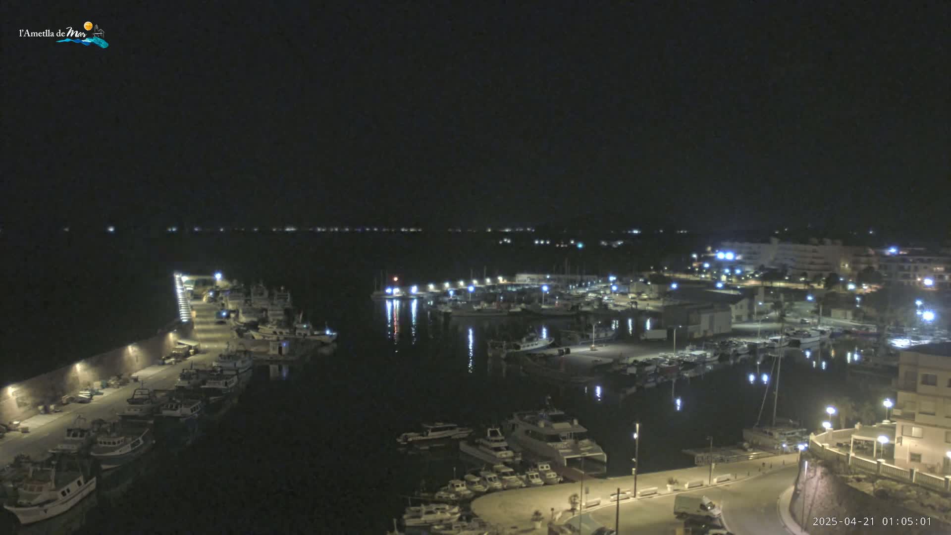 A nighttime view of a harbor filled with numerous boats and surrounded by buildings under a clear, dark sky.