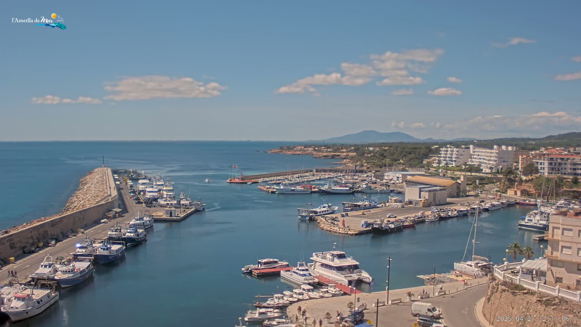 A harbor filled with numerous boats and yachts is situated along a coastline under a partly cloudy sky.
