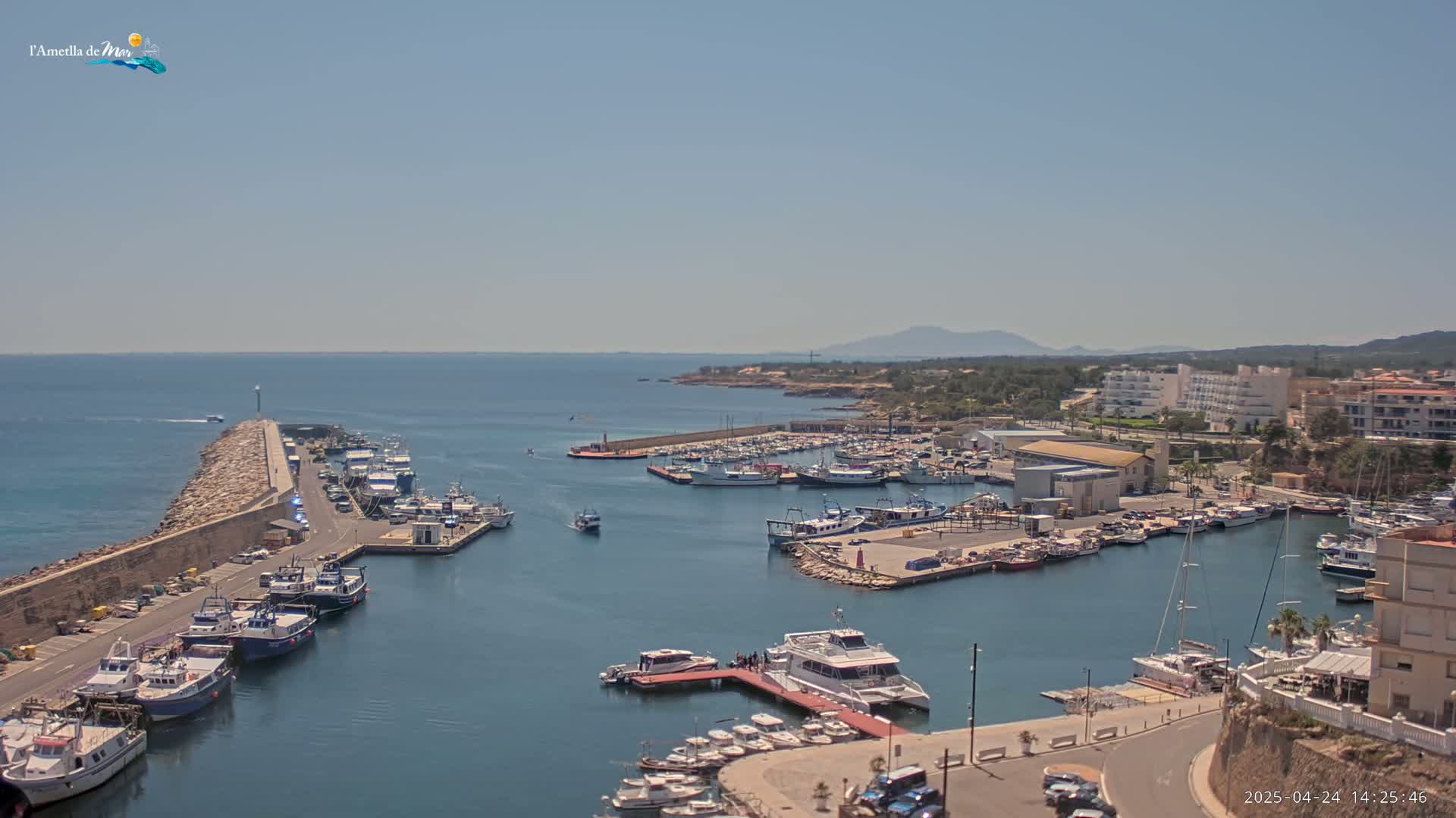 A sunny day reveals a harbor filled with numerous boats and yachts, nestled beside a coastal town under a clear sky.