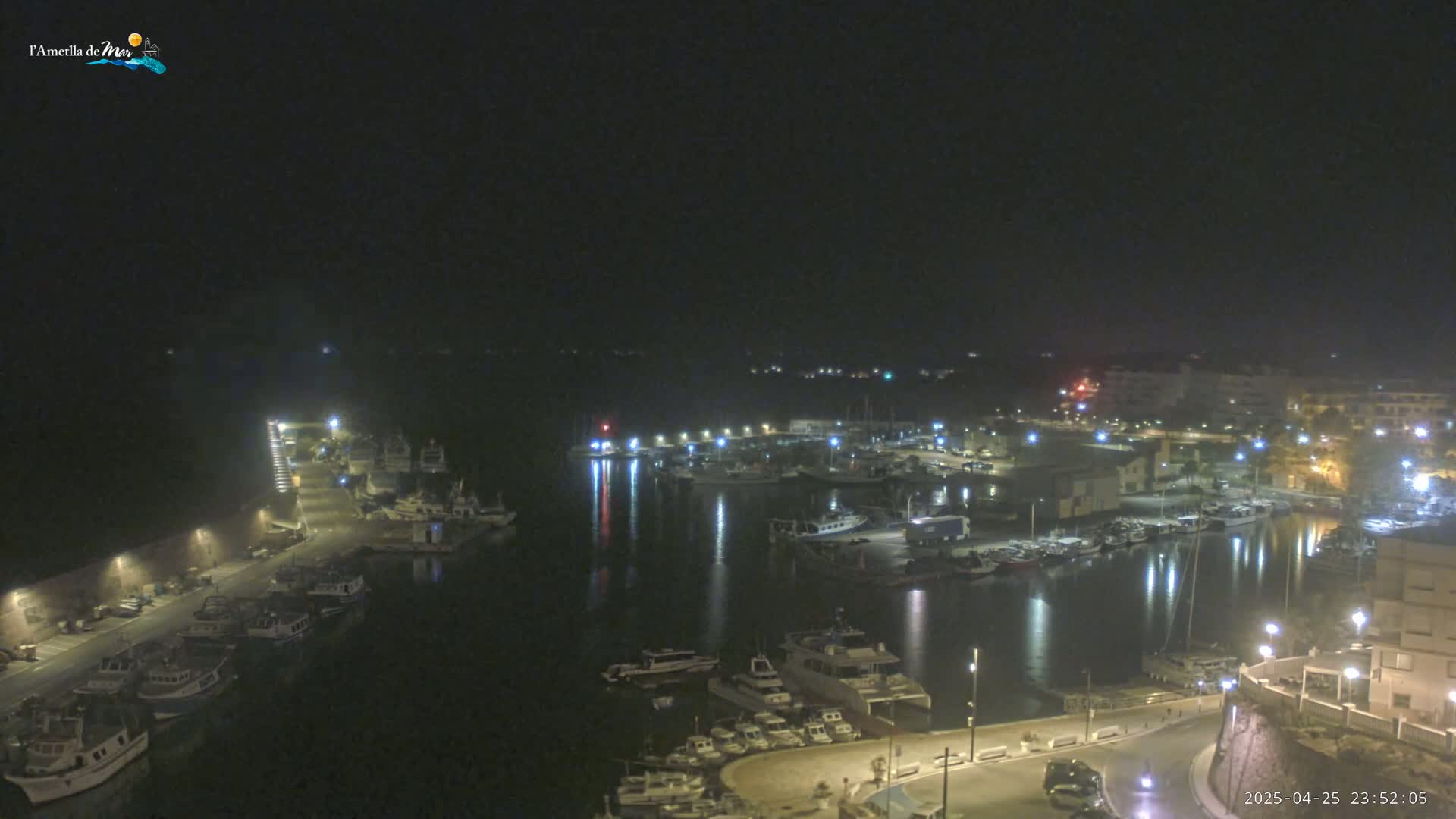 A nighttime view of a harbor filled with boats, illuminated by streetlights and building lights under a dark sky.