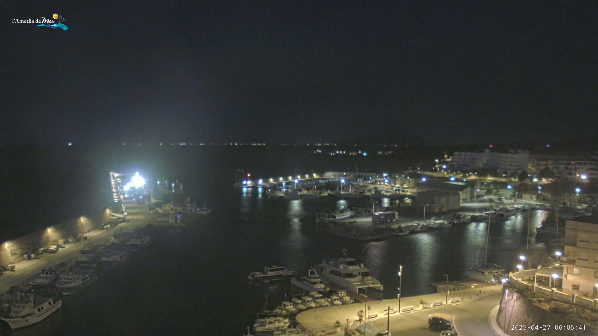 A nighttime, aerial view of a harbor filled with boats, illuminated by streetlights and the lights of the docked vessels under a clear, dark sky.