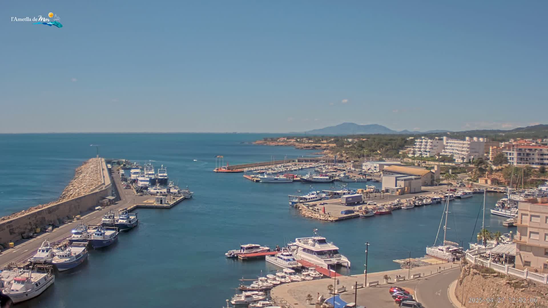 A sunny day reveals a harbor filled with numerous boats and yachts, nestled beside a coastal town under a clear blue sky.