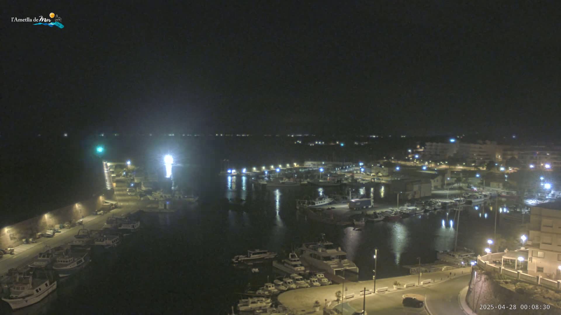 A nighttime view of a harbor filled with boats, illuminated by lights from the docks and buildings on shore.