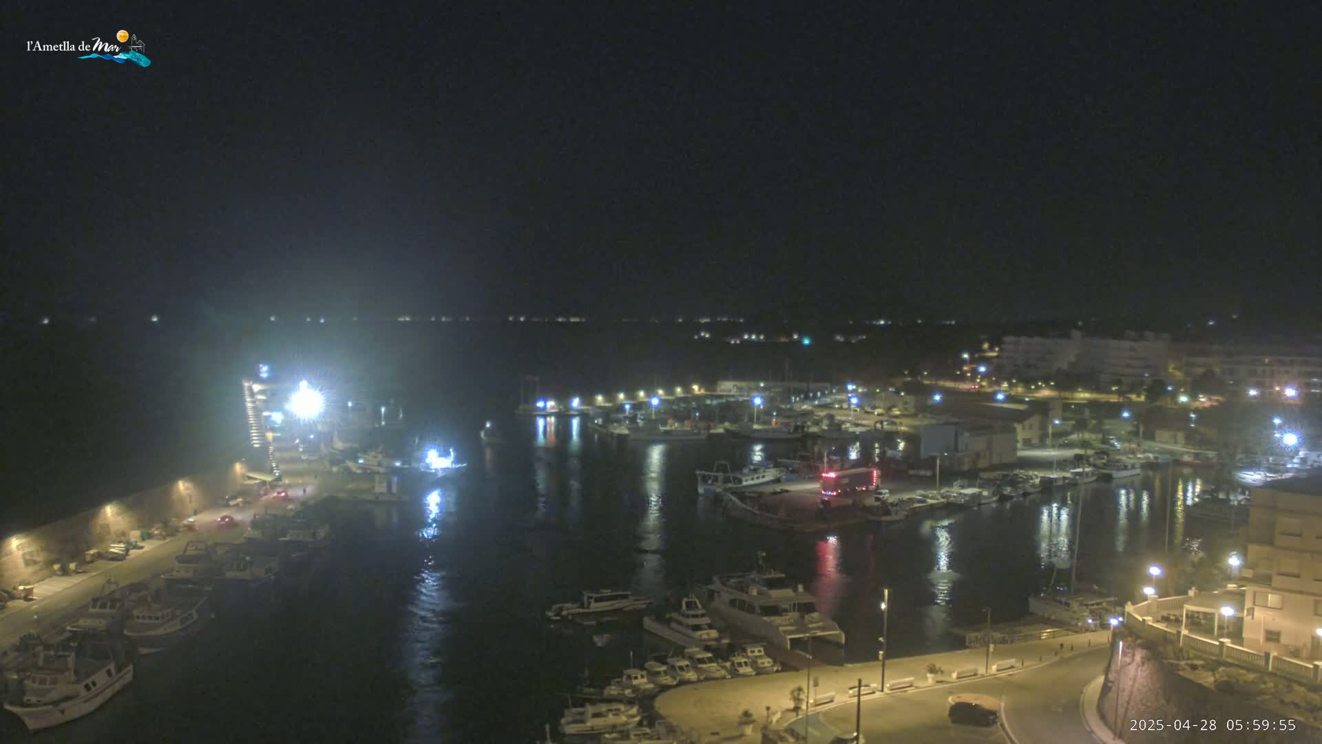 A nighttime, high-angle view of a harbor filled with boats, illuminated by lights, with a town visible in the background.
