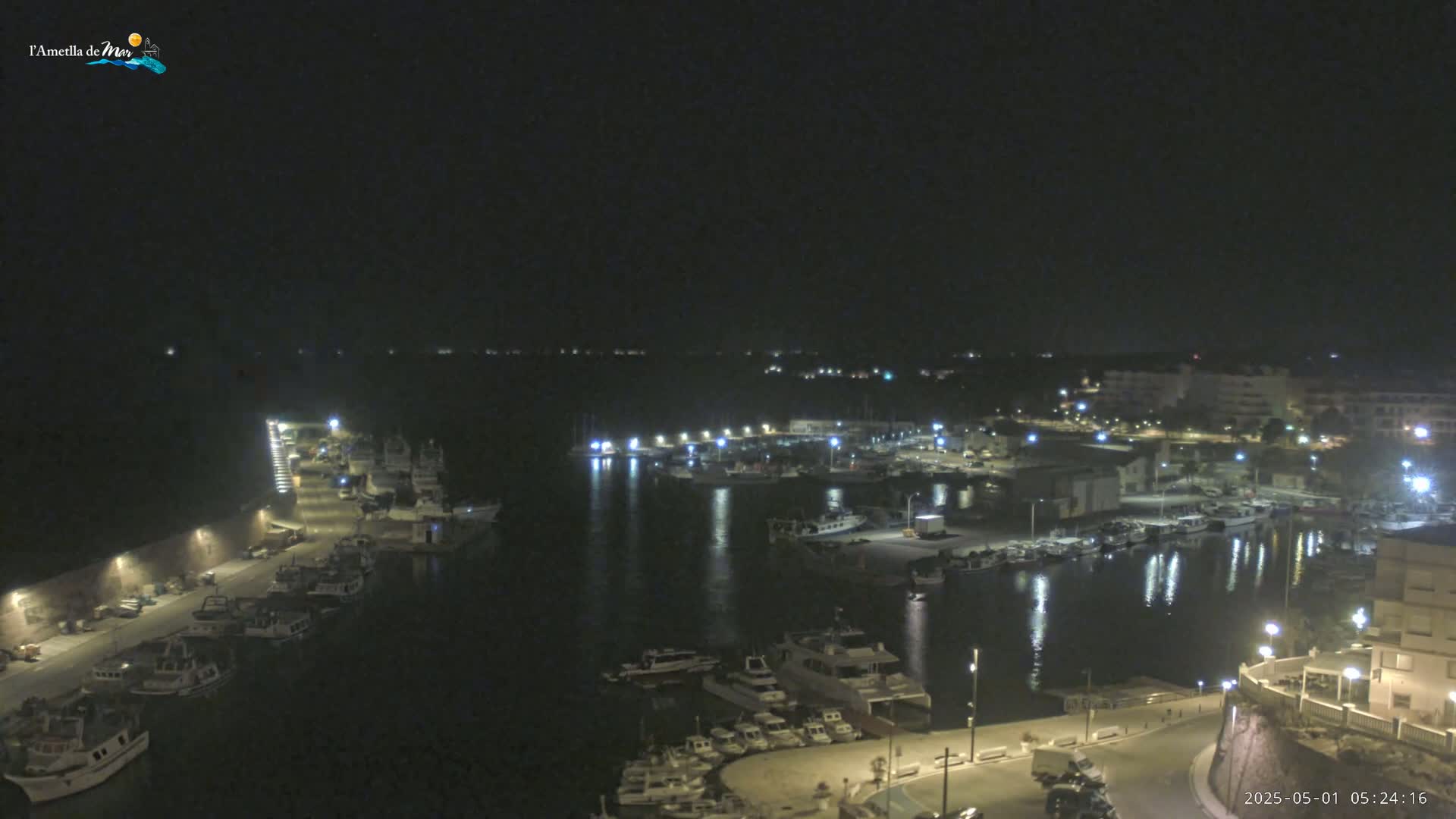A nighttime view of a harbor filled with boats, illuminated by lights along the docks and buildings.