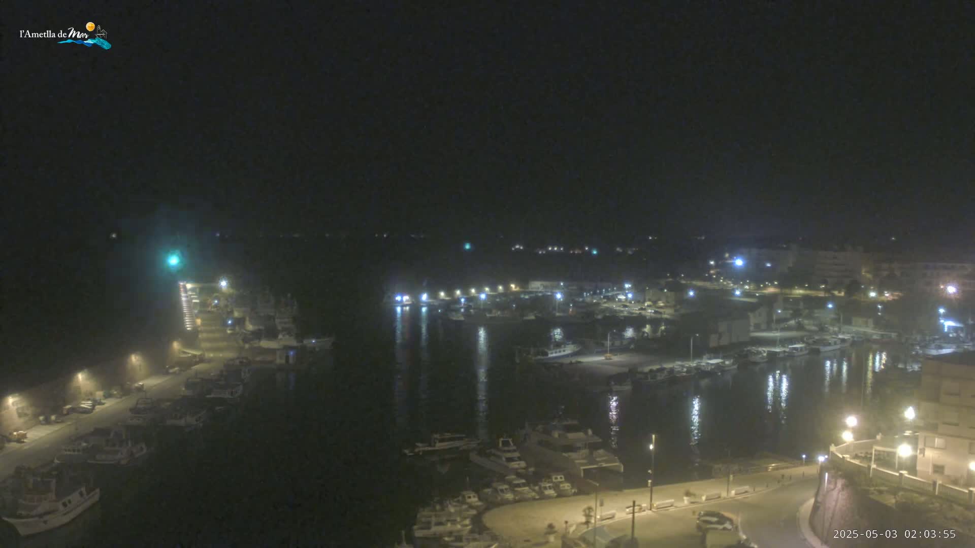 A nighttime, aerial view of a harbor filled with boats, illuminated by streetlights and building lights under a dark sky.