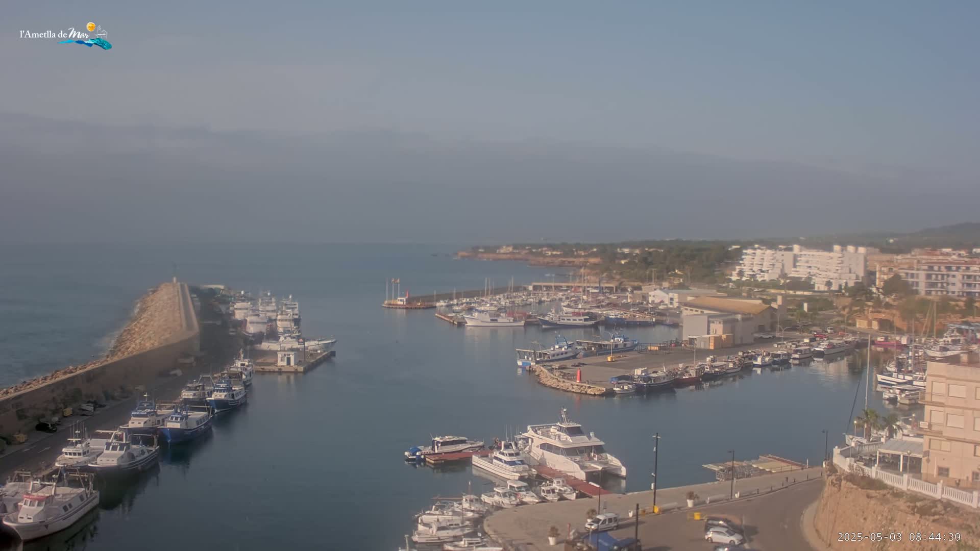 A hazy morning view of a harbor filled with numerous boats and yachts, situated next to a coastal town.