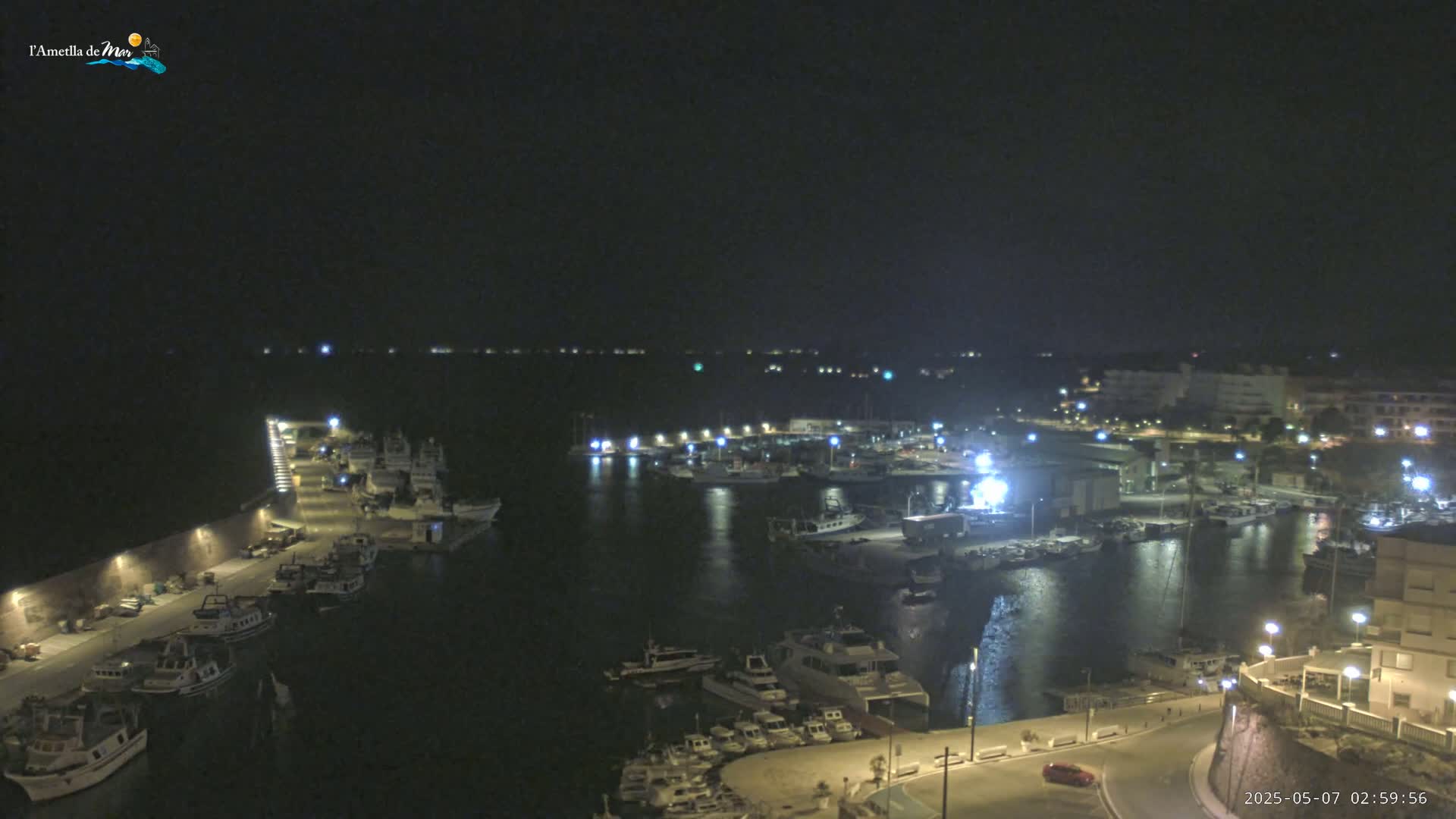A nighttime view of a harbor filled with numerous boats and illuminated buildings, under a clear, dark sky.