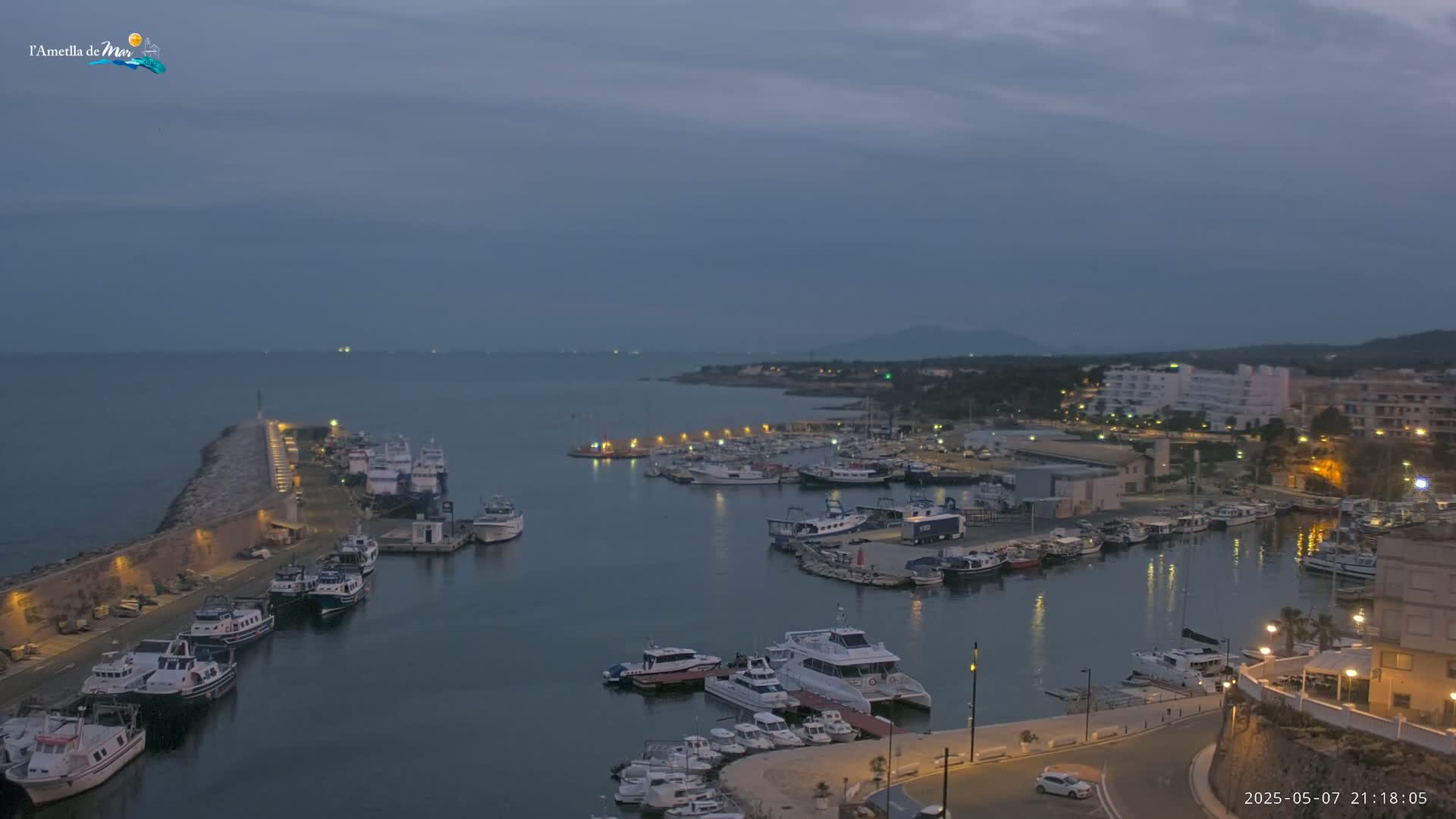 A harbor filled with boats is illuminated at twilight under a cloudy sky.