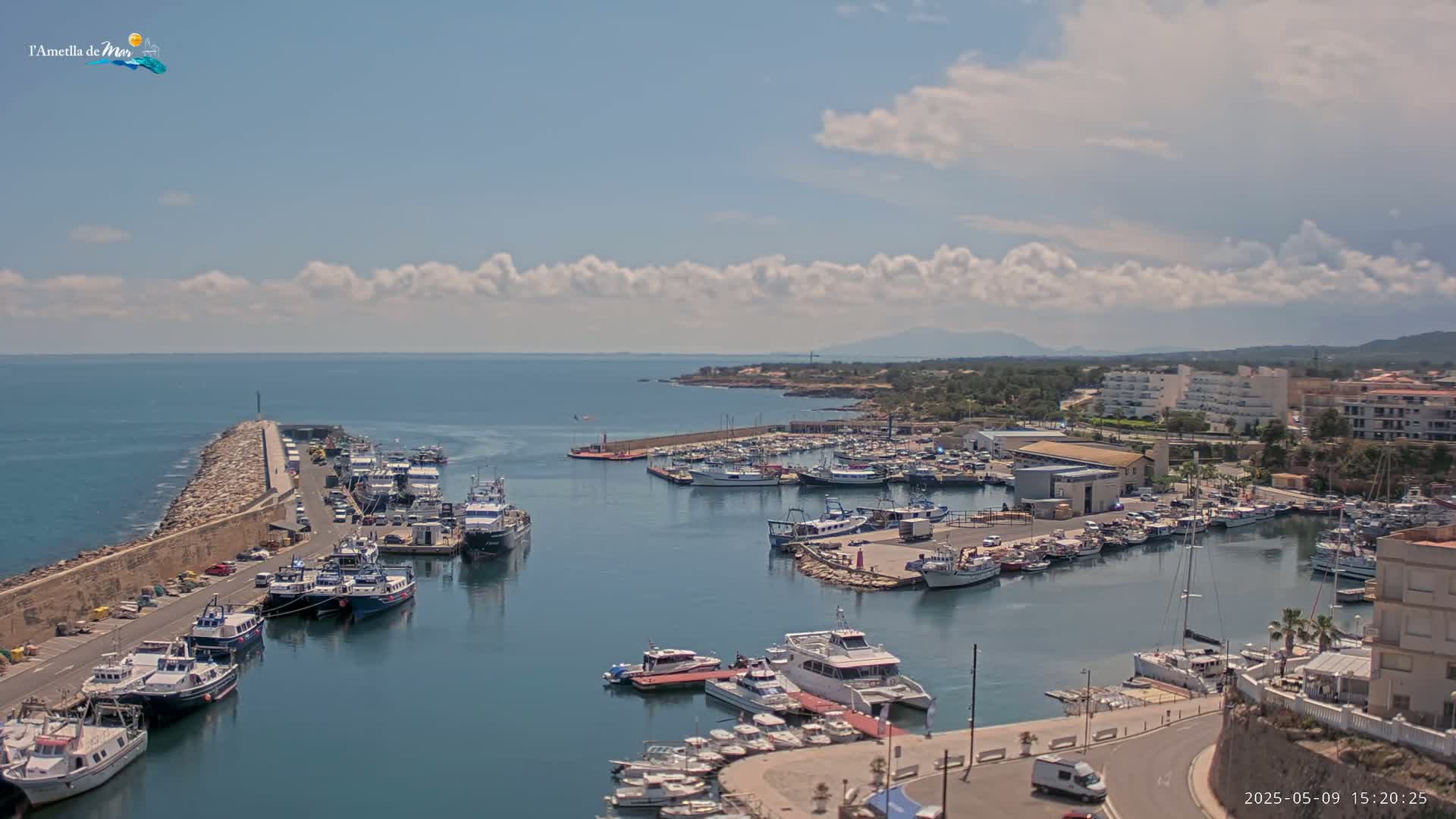 A harbor filled with numerous boats and yachts is nestled beside a town under a partly cloudy sky.