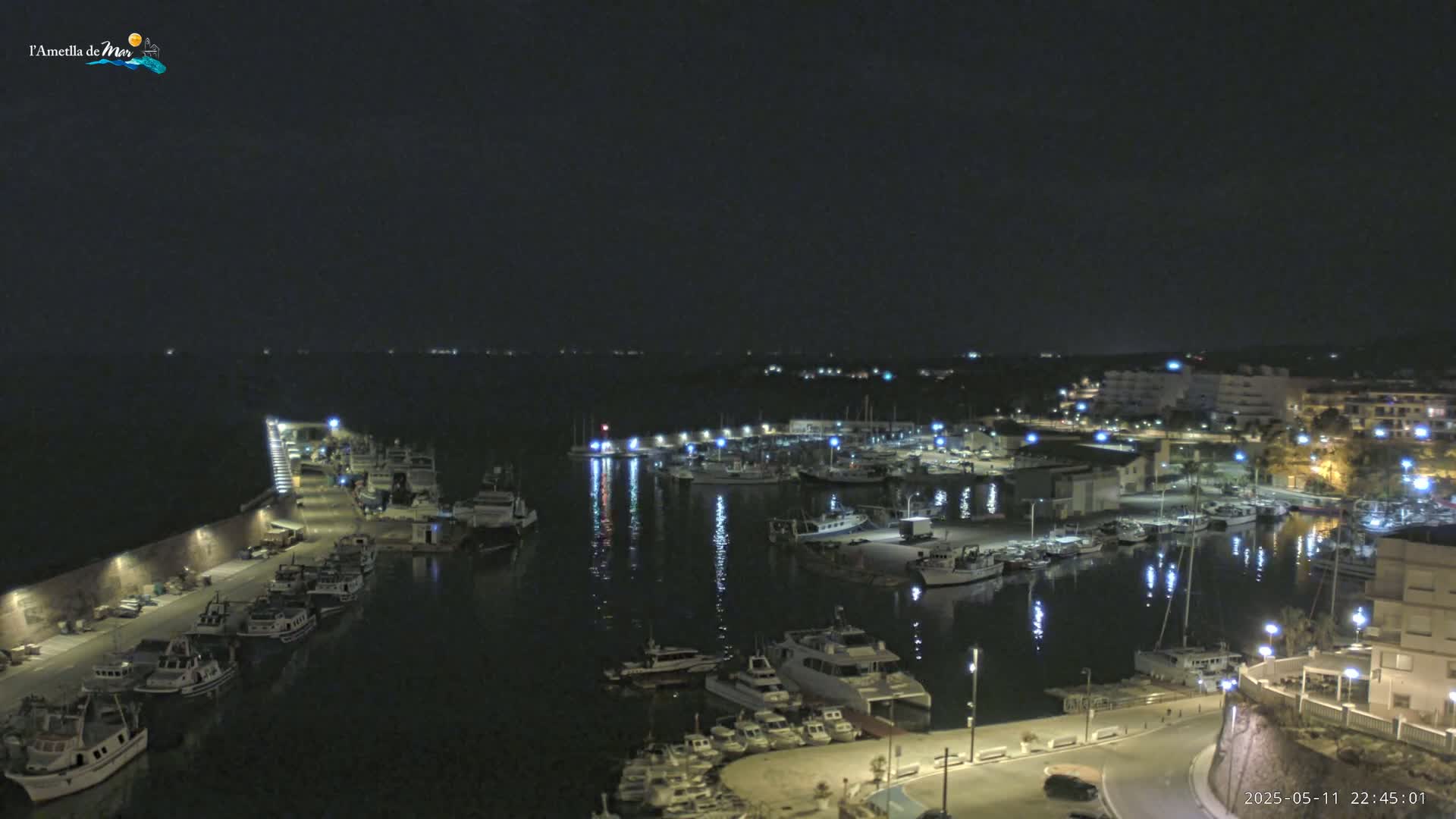 A nighttime view of a harbor filled with boats, illuminated by lights, under a clear, dark sky.