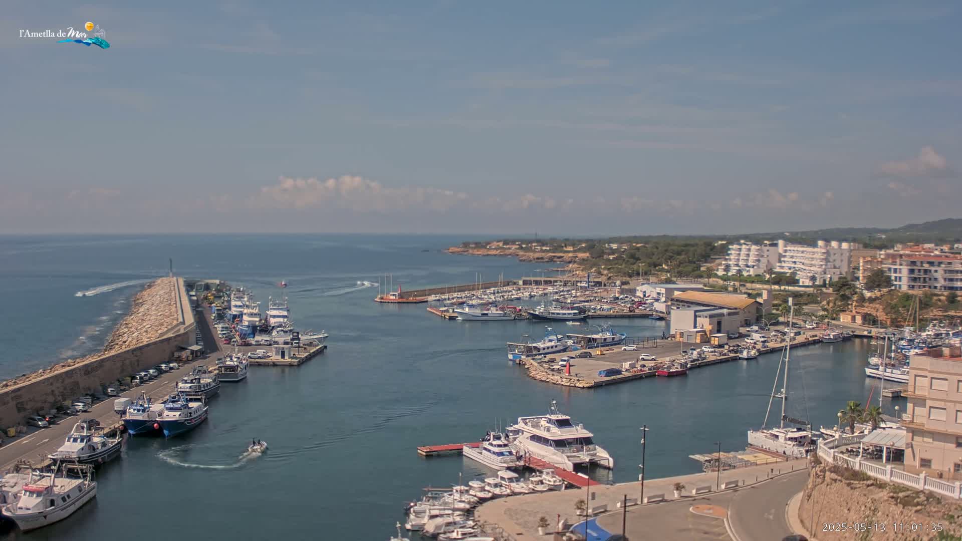 A harbor filled with numerous boats and yachts is situated next to a coastline under a partly cloudy sky.