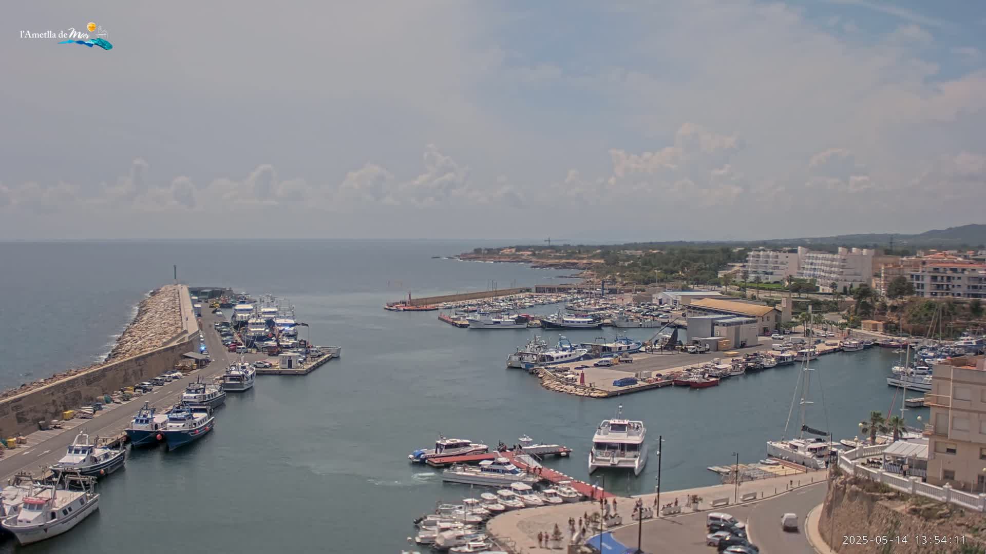 A harbor filled with many boats is situated next to a stone seawall under a partly cloudy sky.