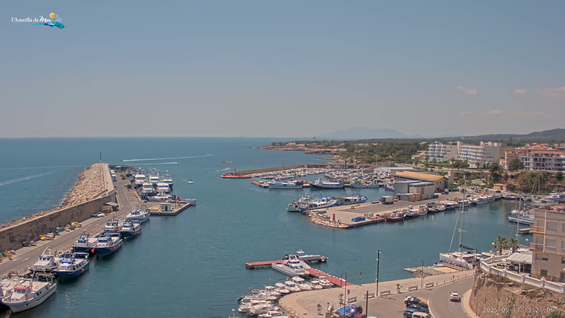 A harbor filled with numerous boats and ships is situated next to a stone breakwater, under a clear sunny sky.