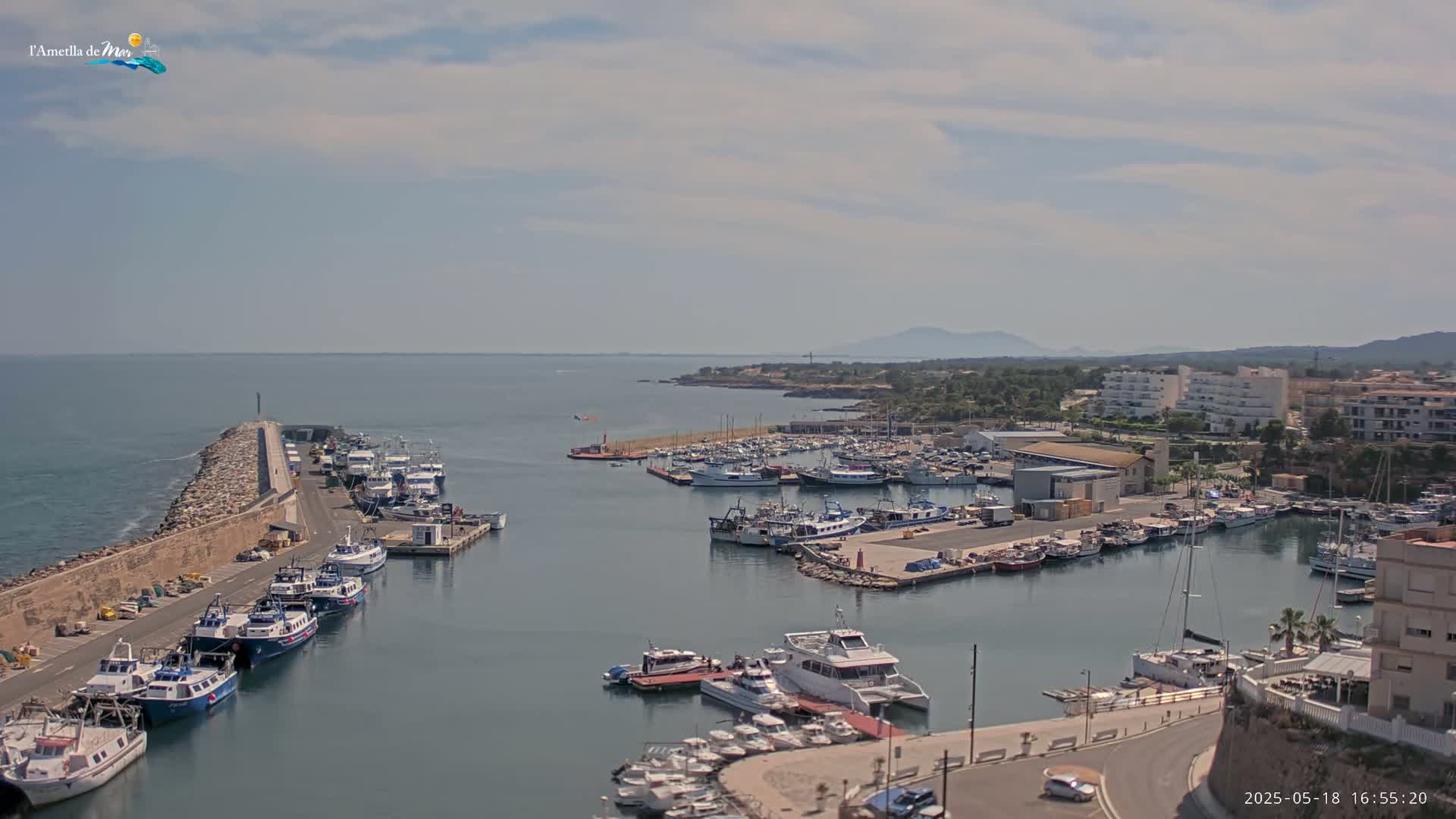 A harbor filled with numerous boats and yachts is situated near a coastline under a partly cloudy sky.