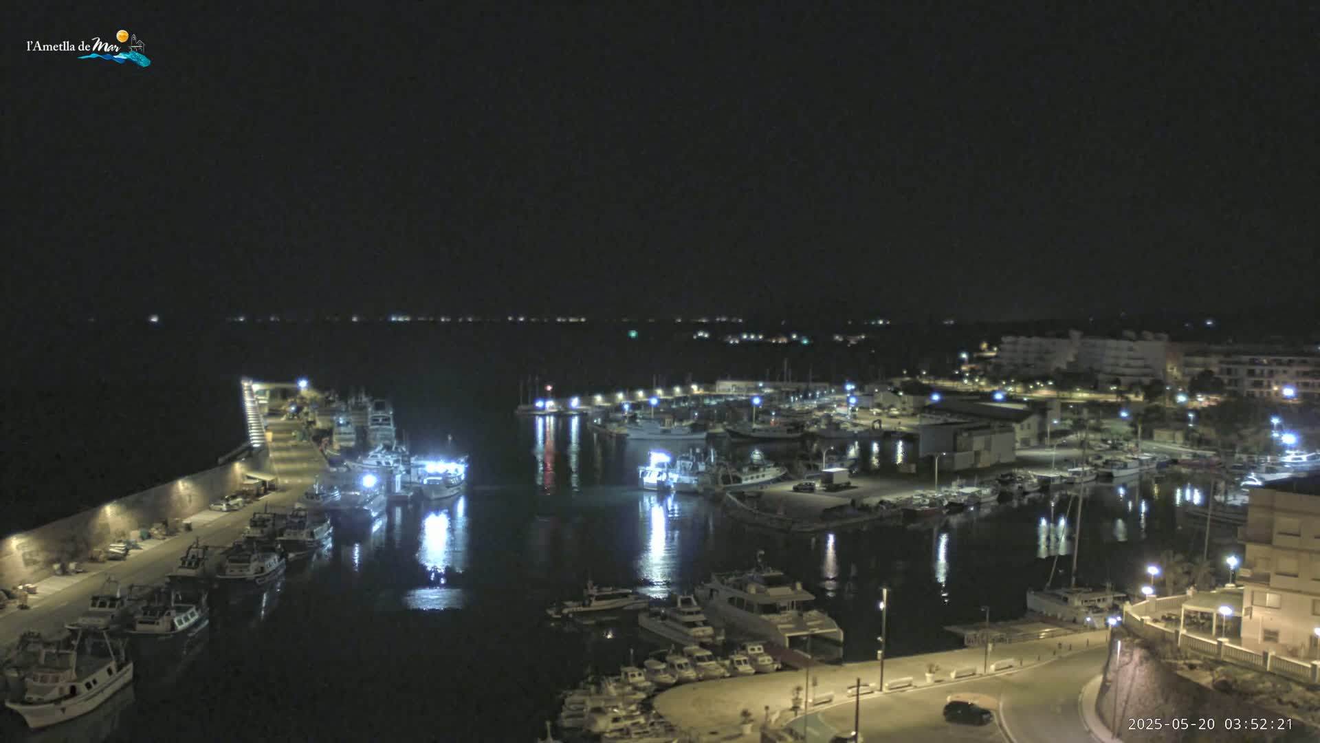 A nighttime view of a harbor filled with boats, illuminated by lights, under a clear, dark sky.