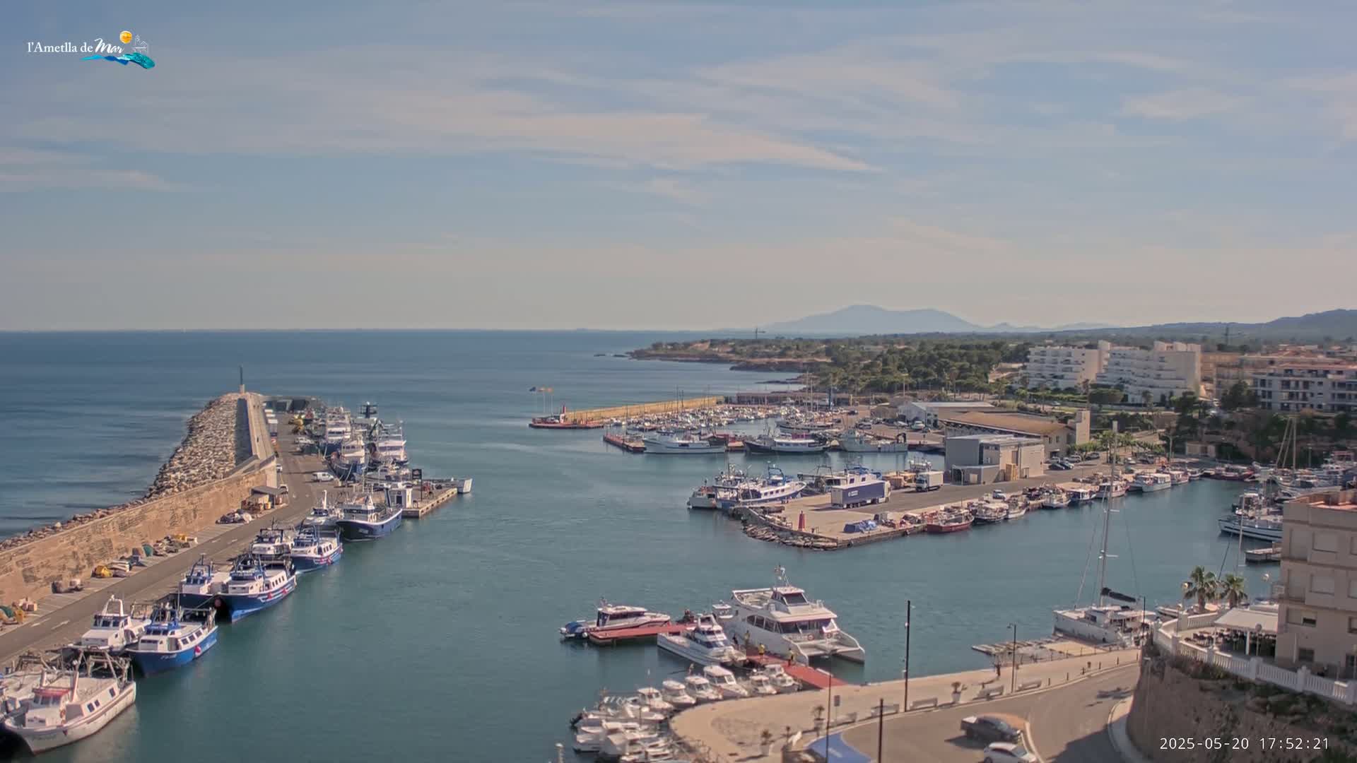 A harbor filled with many boats of various sizes is situated next to a coastal town under a partly cloudy sky.