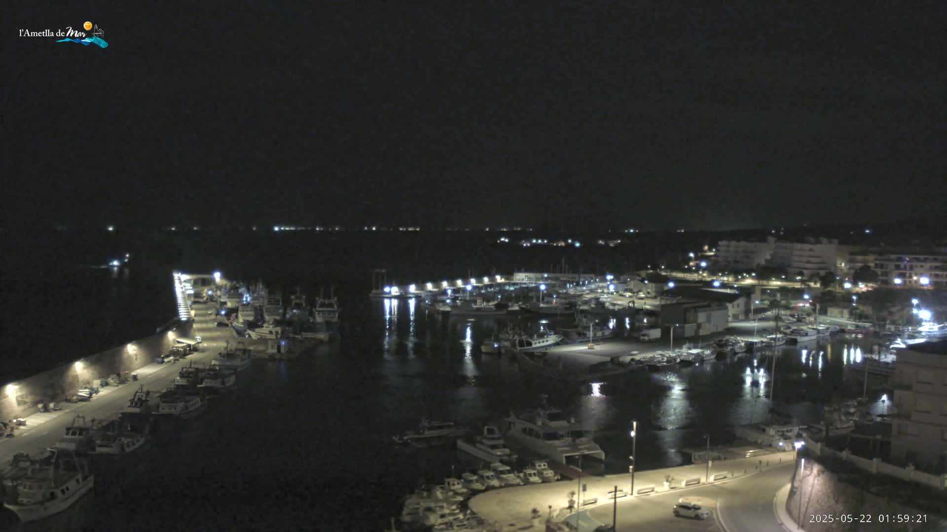 A nighttime, aerial view of a harbor filled with boats, illuminated by lights along a waterfront with buildings in the background.