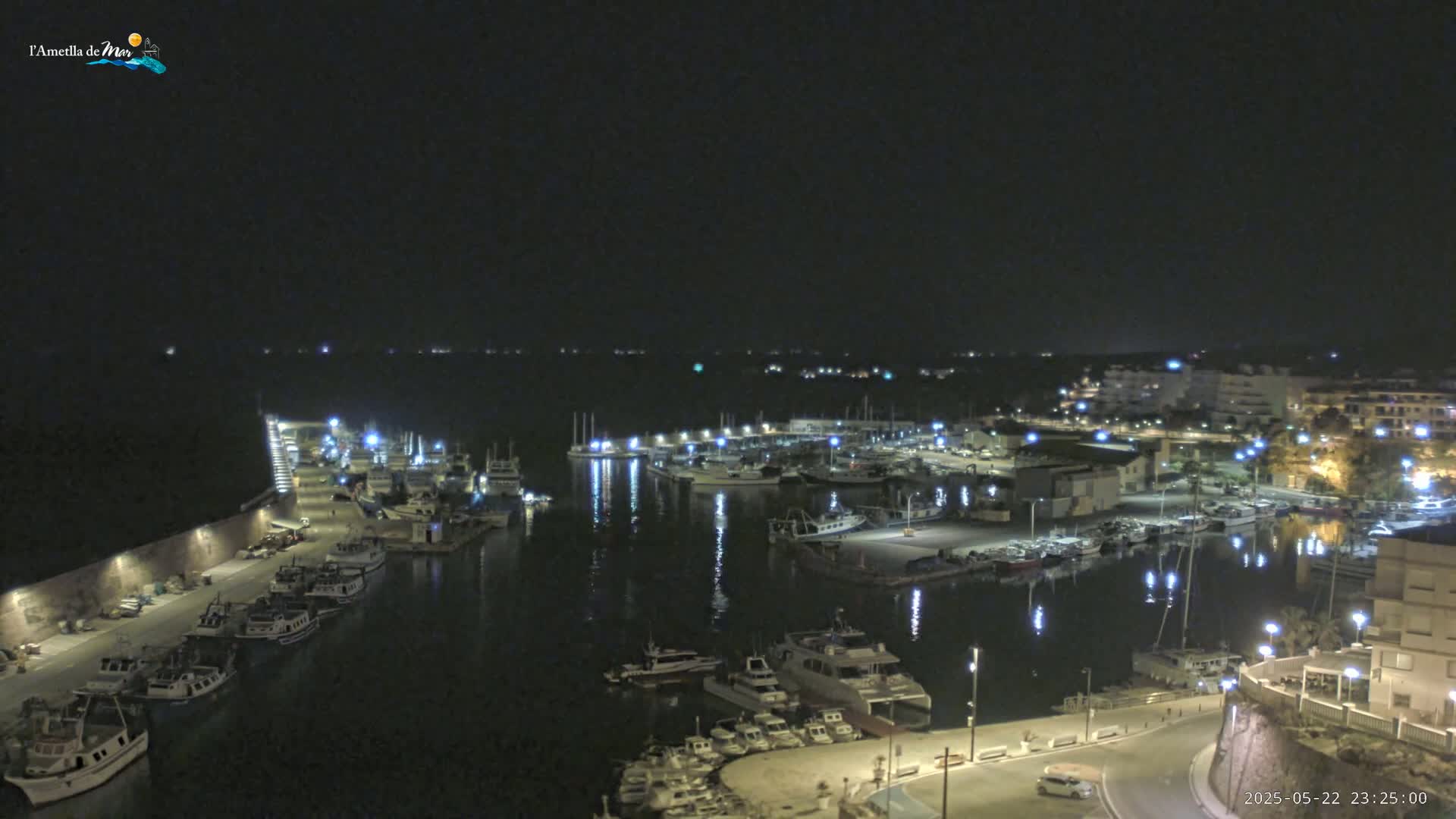 A nighttime view of a harbor filled with numerous boats and illuminated by lights, with a calm body of water reflecting the lights.