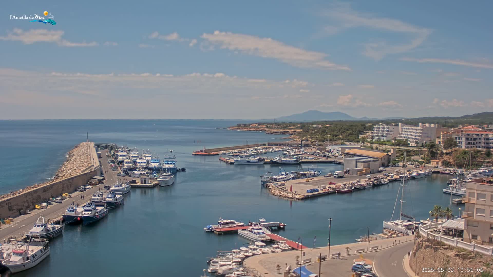 A harbor filled with numerous boats and yachts is situated beside a coastal town under a partly cloudy sky.