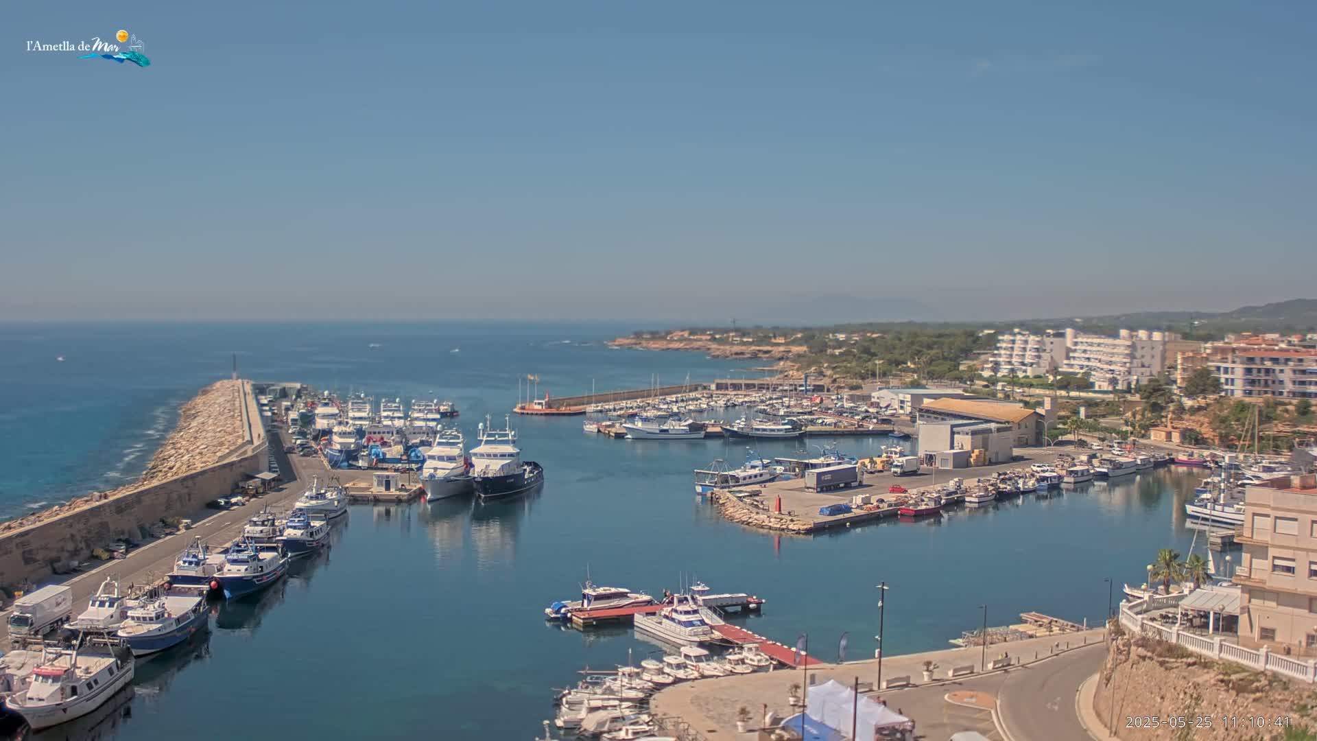 A harbor filled with numerous boats and yachts is situated on a calm, clear day next to a rocky coastline.