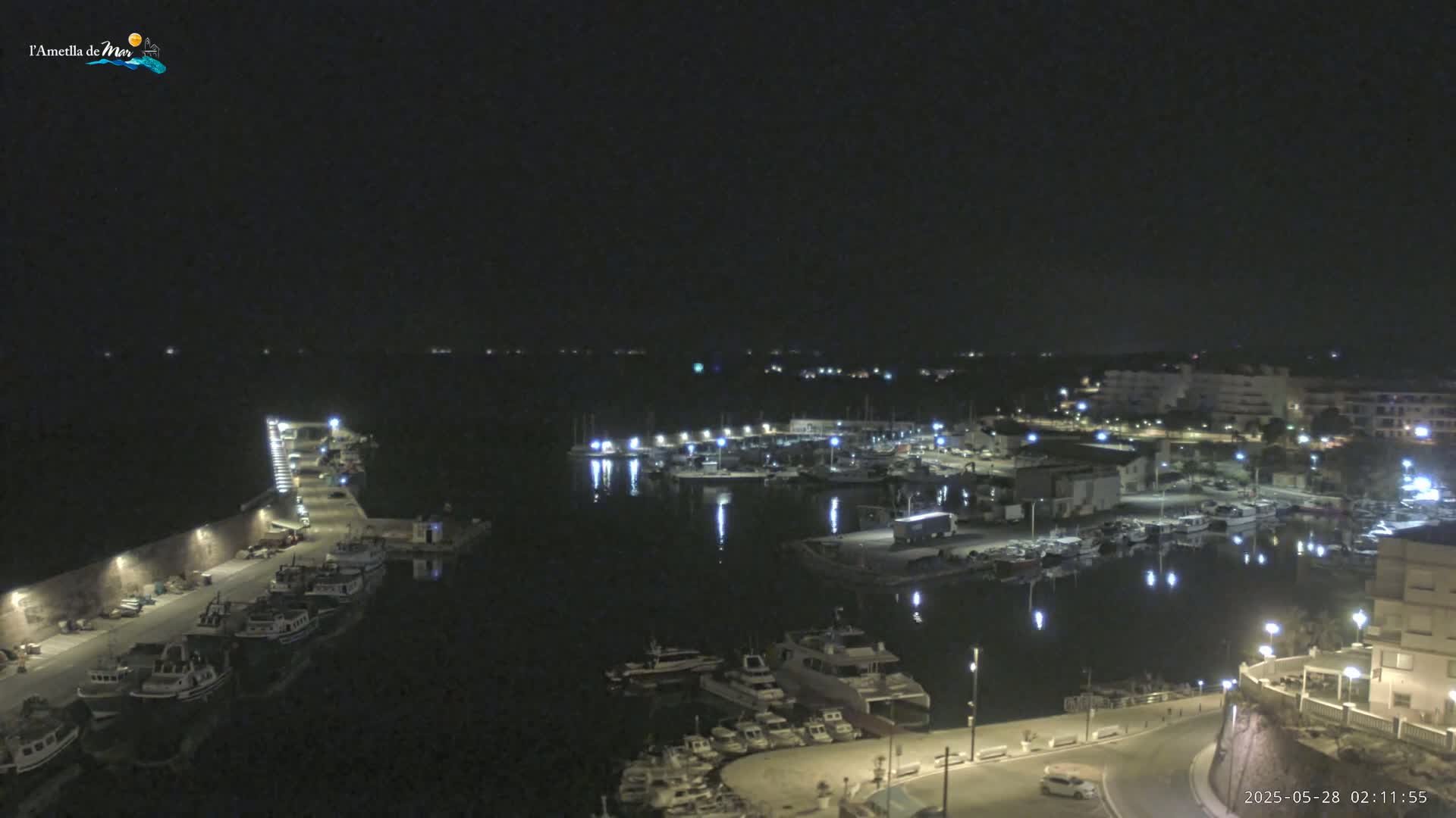 A nighttime, high-angle view of a harbor filled with boats, illuminated by streetlights and building lights, under a clear, dark sky.