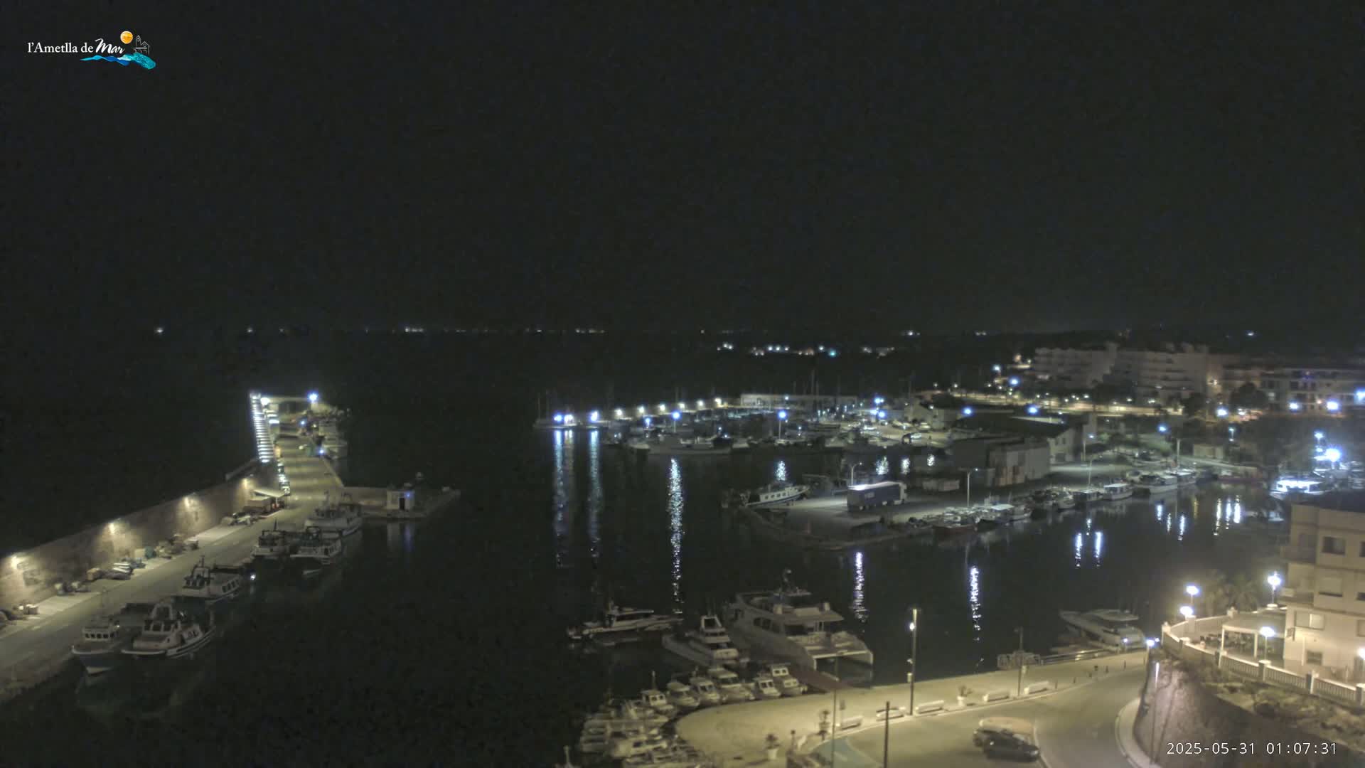 A nighttime aerial view shows a harbor filled with boats, illuminated by lights, under a clear, dark sky.