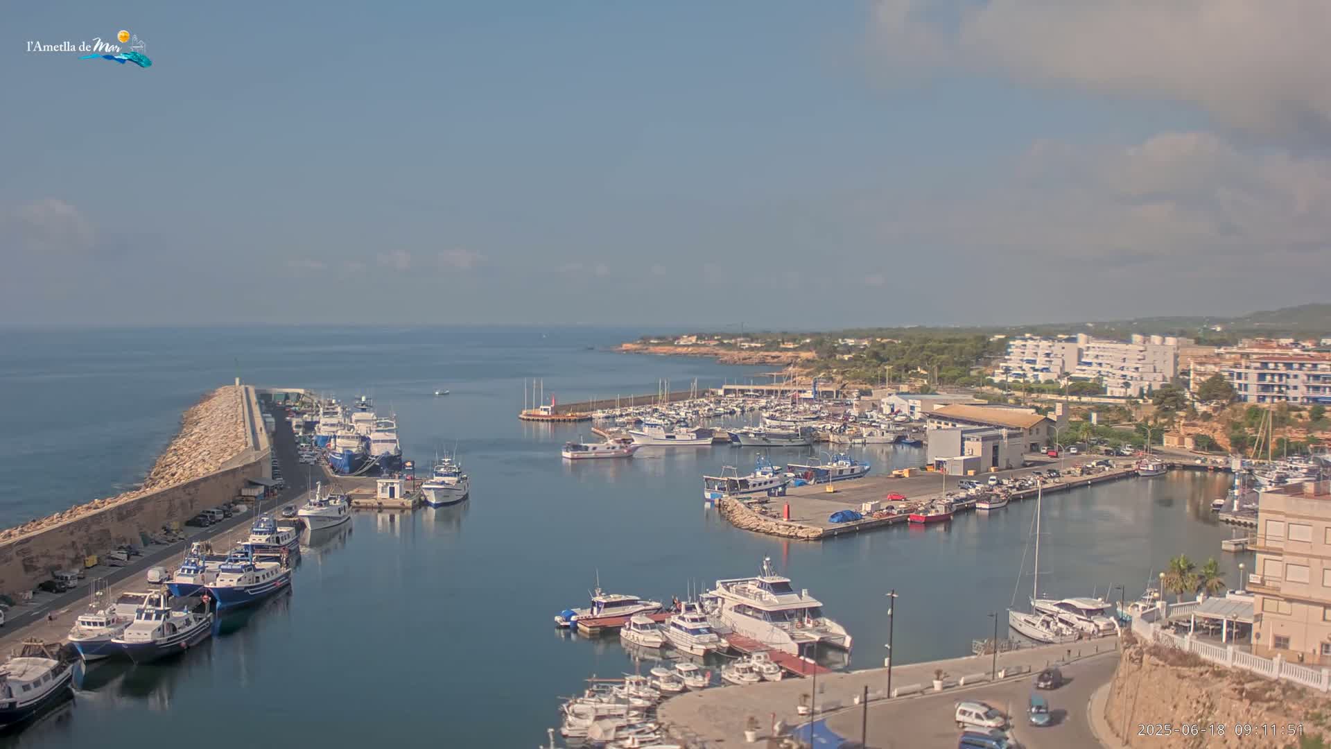 A harbor filled with numerous boats and yachts is situated next to a rocky coastline under a mostly clear sky.