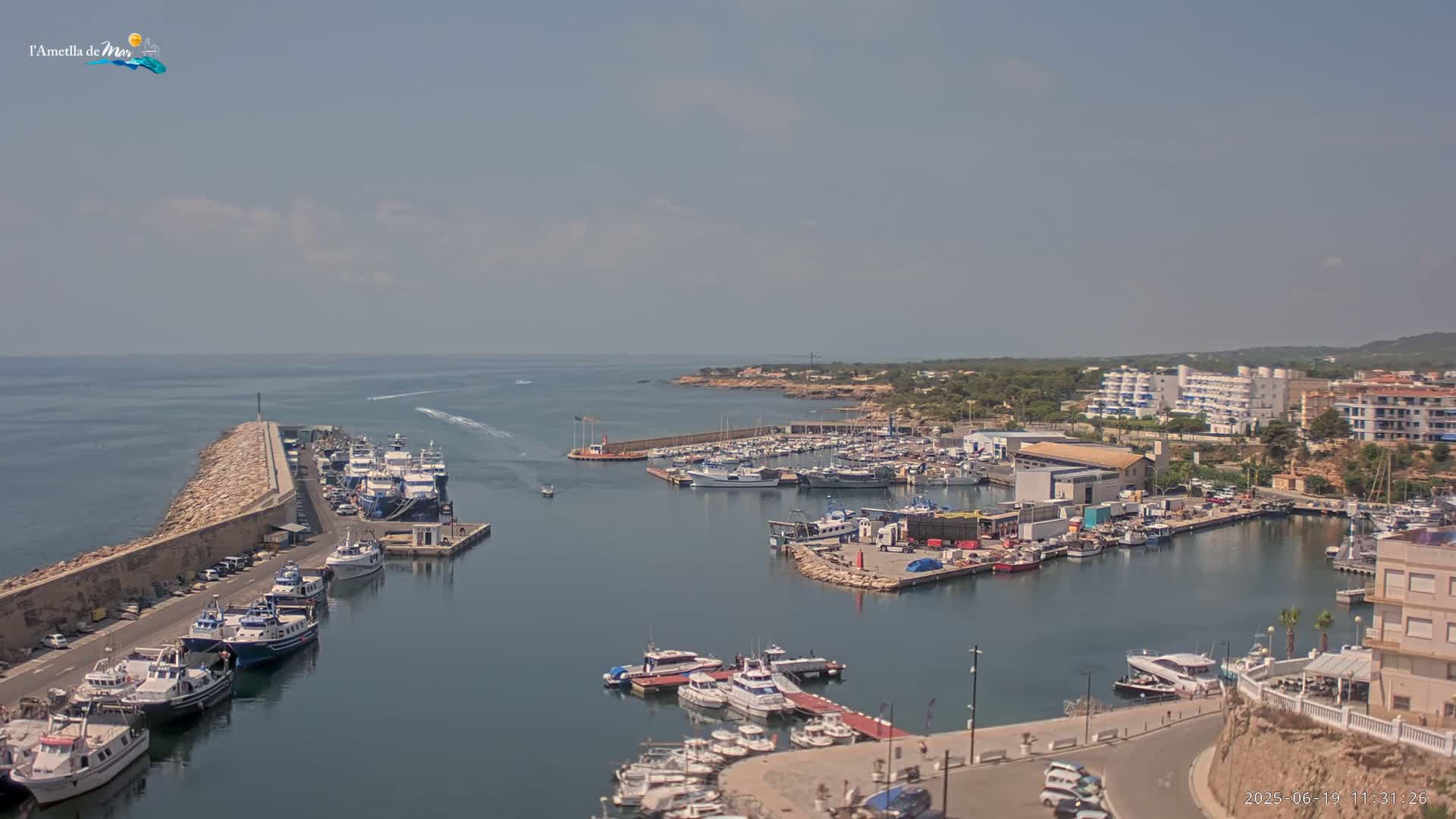 A harbor filled with numerous boats and yachts is situated next to a town under a partly cloudy sky.