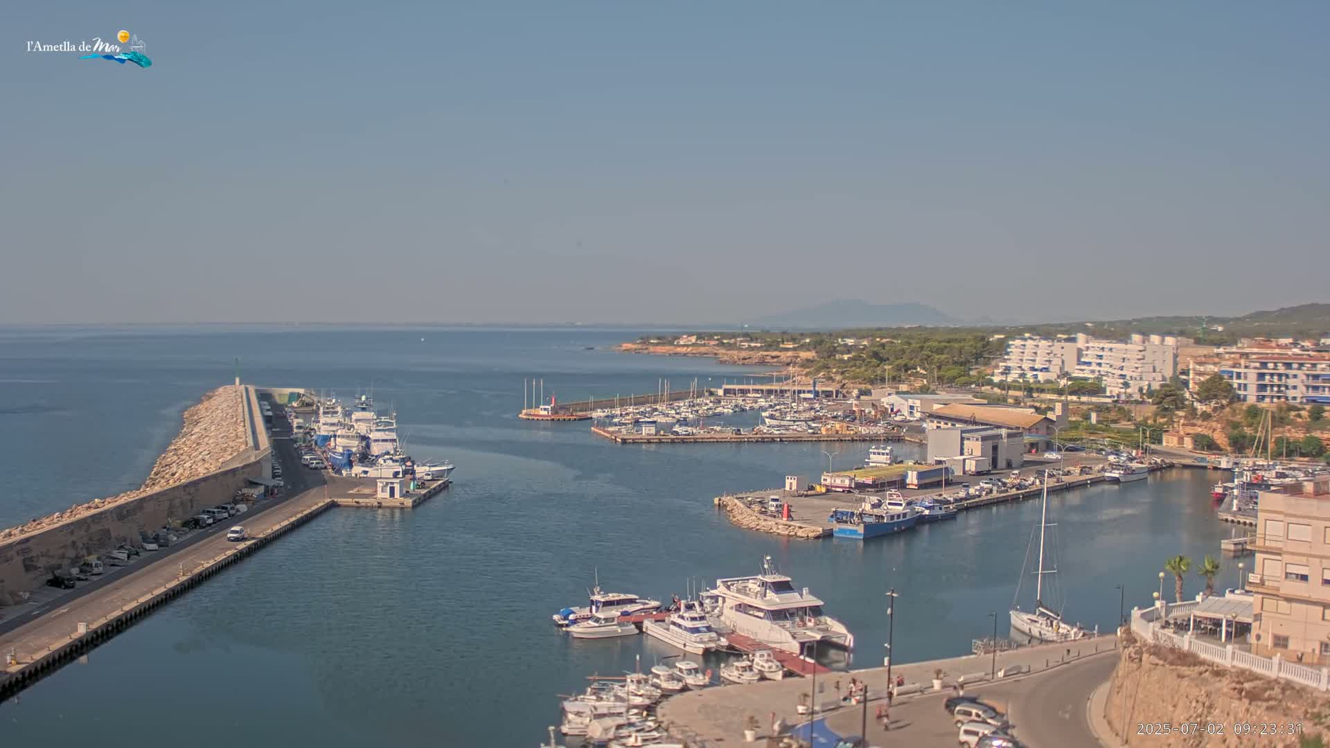 A harbor filled with numerous boats and yachts is situated along a coastline on a clear, sunny day.