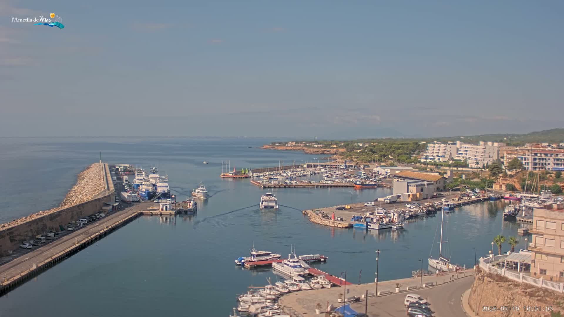 A harbor filled with numerous boats and yachts is situated next to a seaside town under a clear, sunny sky.