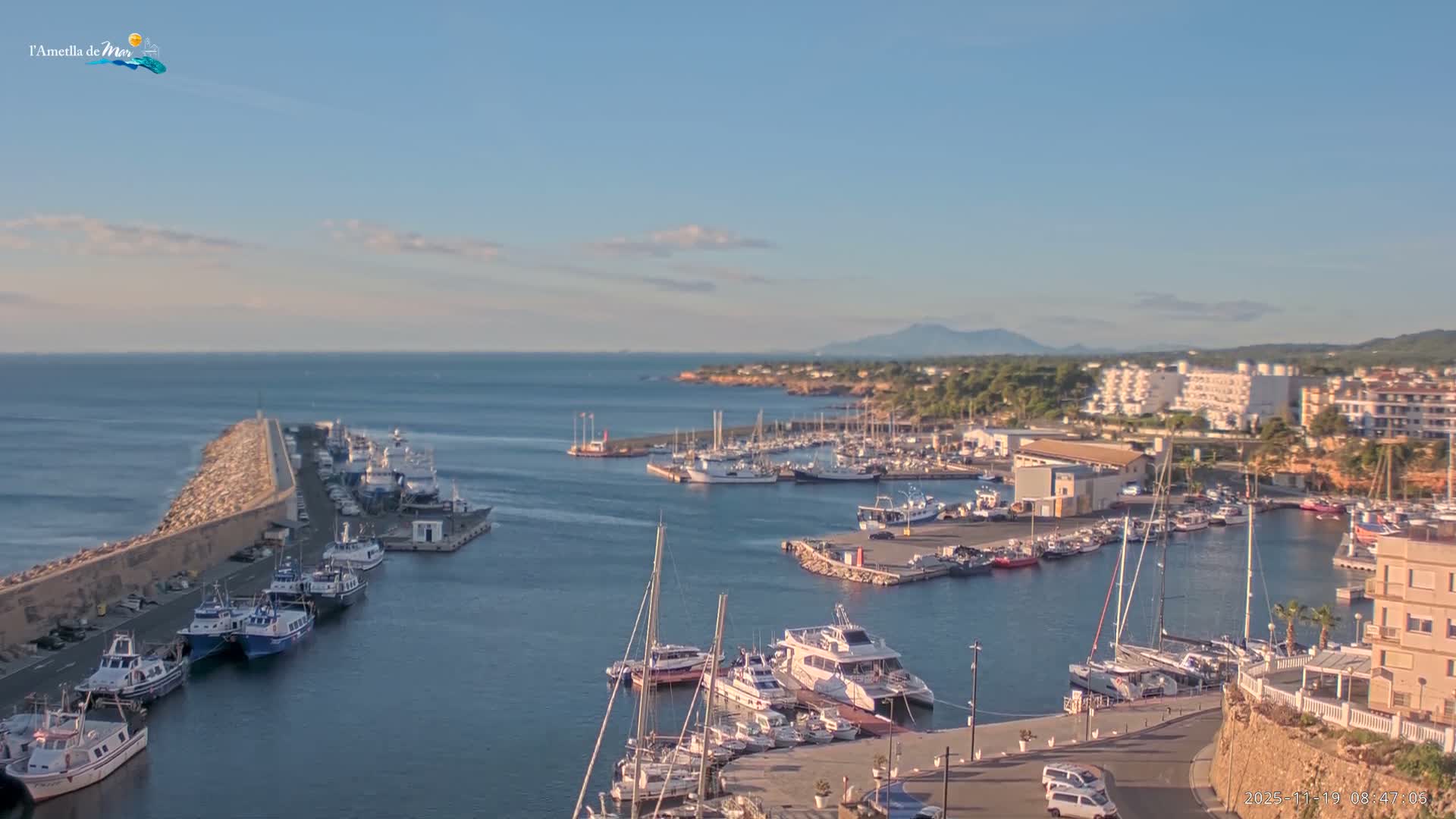 A nighttime aerial view shows a harbor filled with boats, illuminated by lights along the docks and buildings surrounding the calm water.