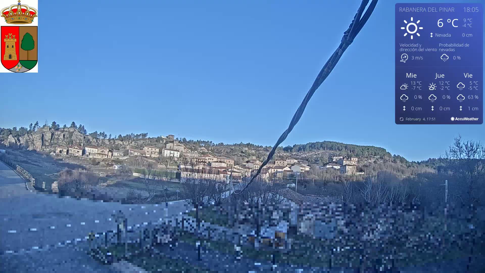 A small village nestled in a rocky hillside is visible under a clear blue sky.
