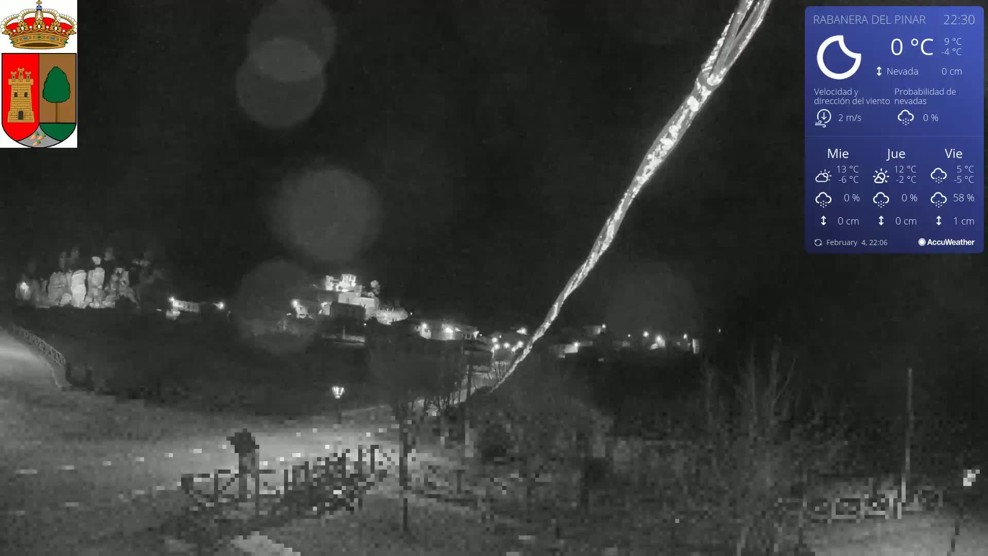 A nighttime, snowy scene of a small town illuminated by streetlights, with a faint light streak across the sky.