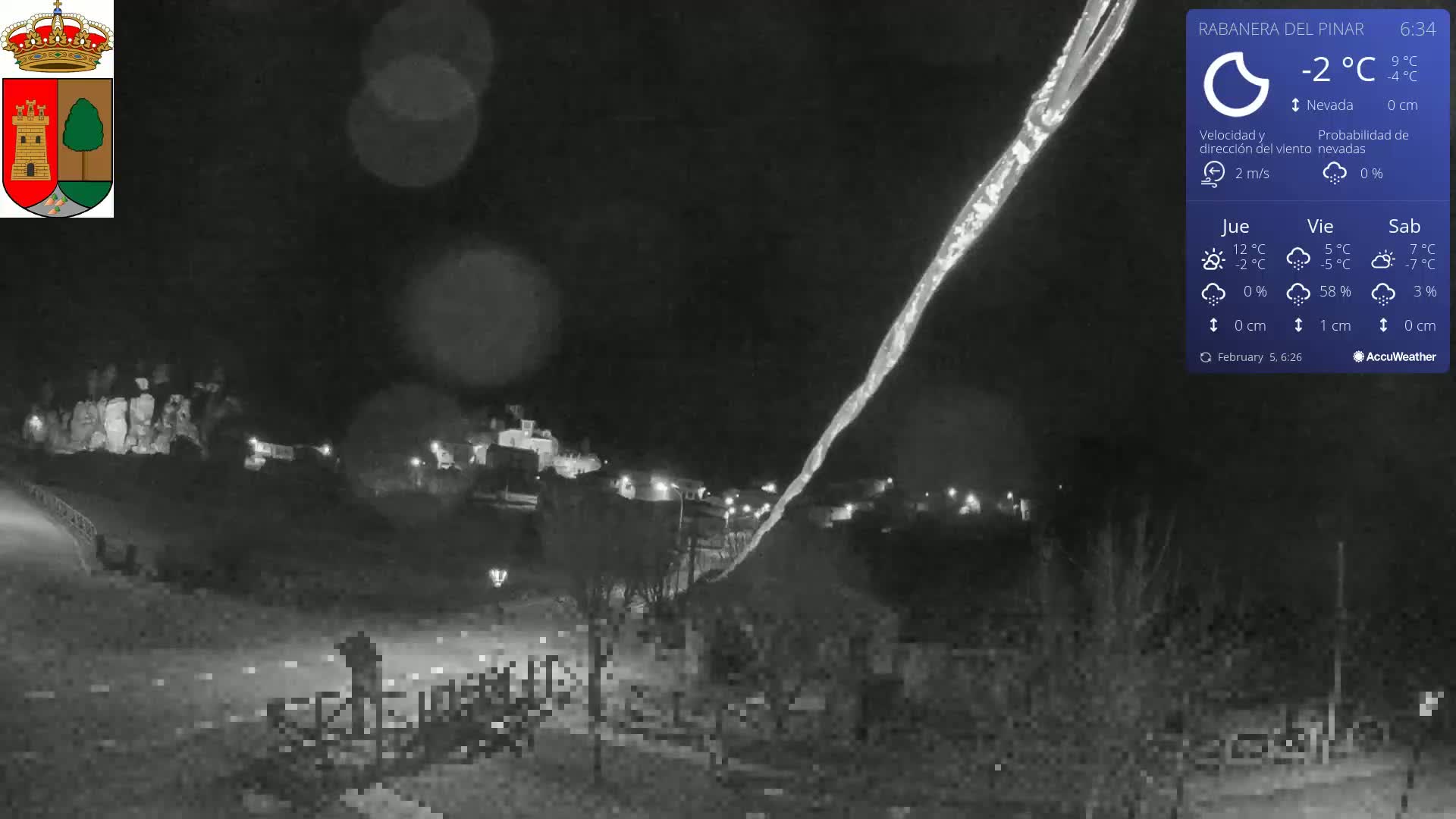 A nighttime, snowy scene shows a small village illuminated with faint lights, a long icicle hanging down from above, and a dark, mostly empty foreground.
