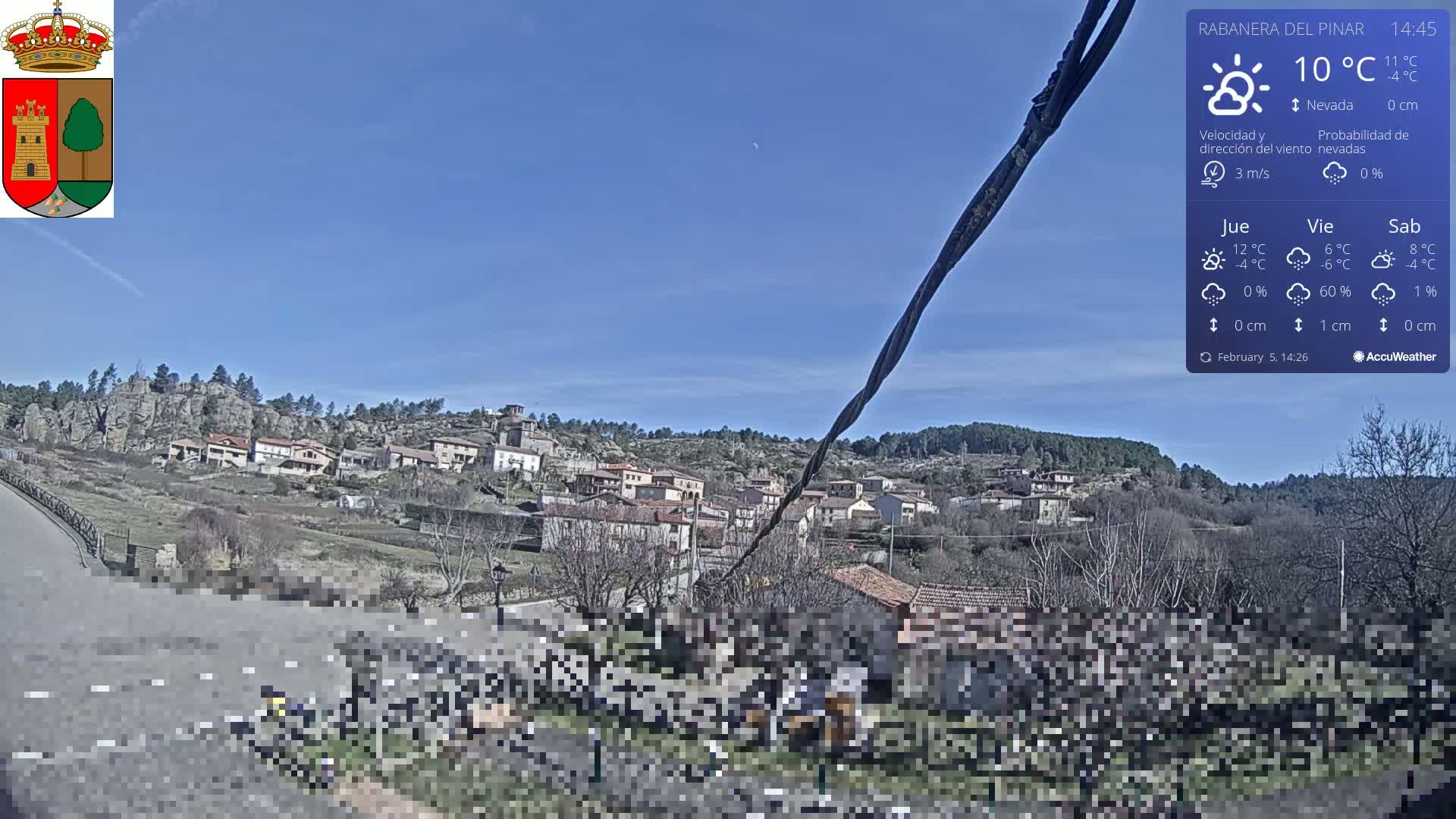A small village nestled on a hillside under a clear blue sky is viewed from a road below.