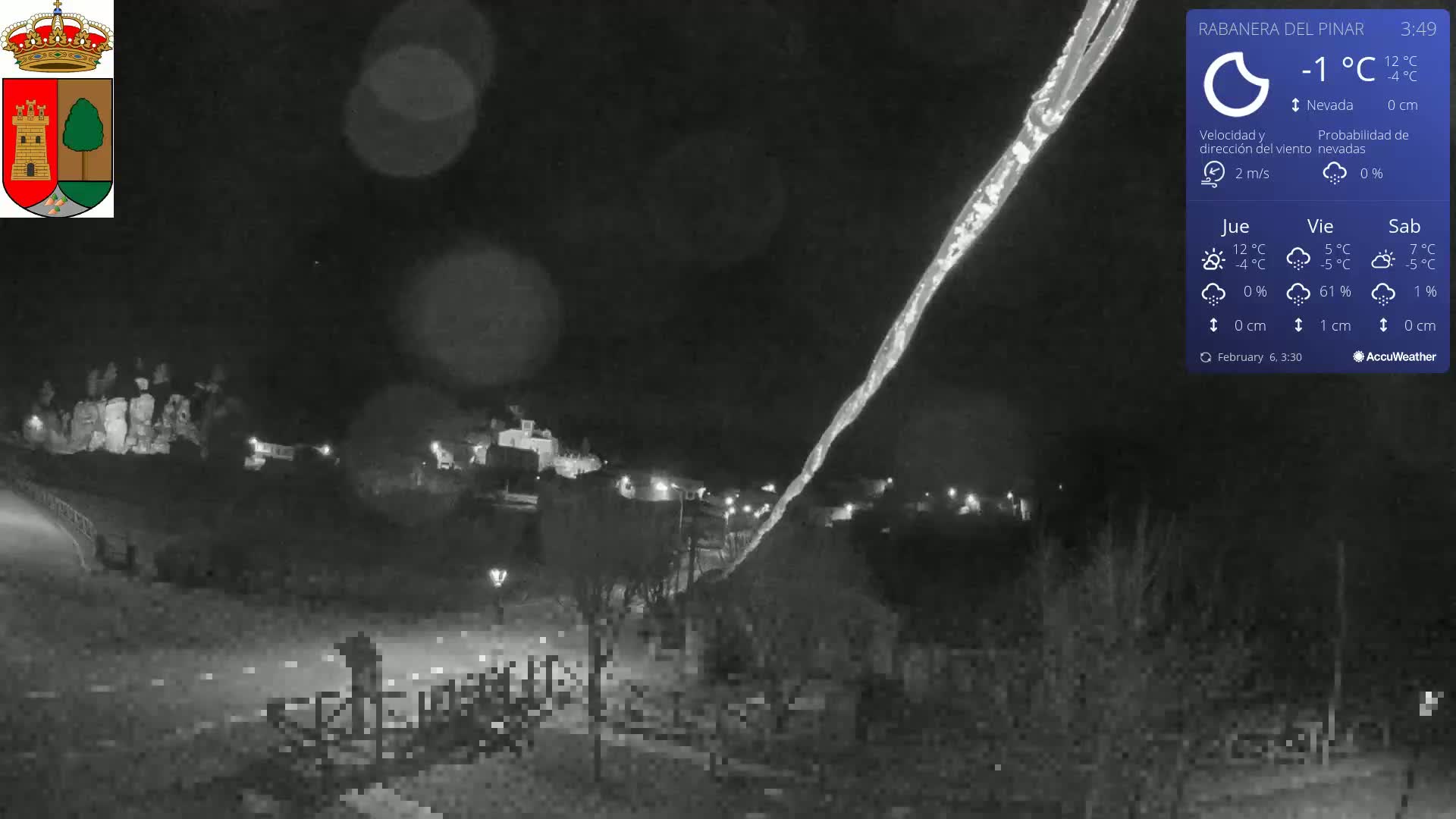 A nighttime, low-light view of a town in snowy conditions, with a long, bright streak in the sky possibly from a light source.