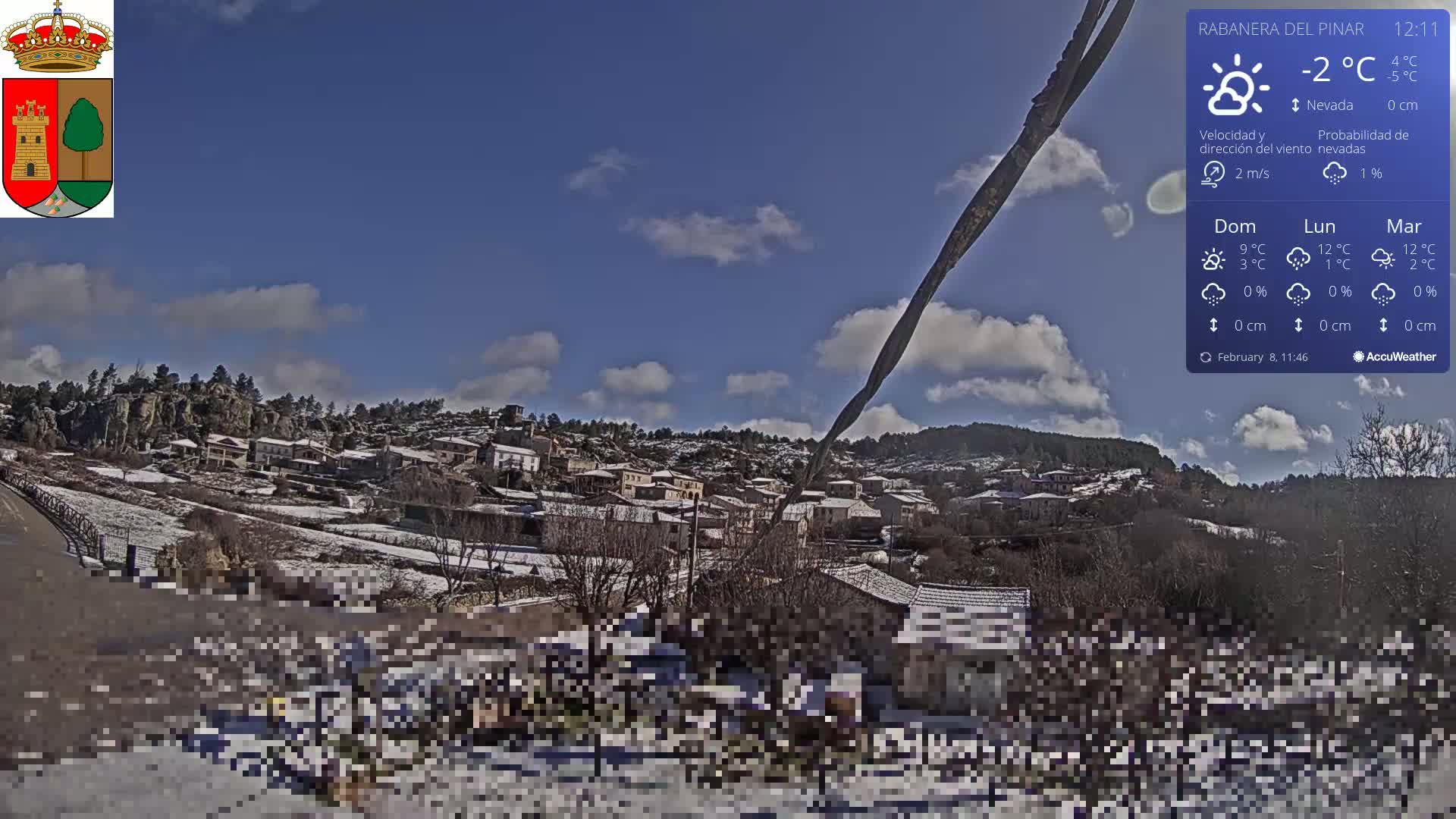 A snow-covered village sits on a hillside under a mostly sunny sky with a few clouds.