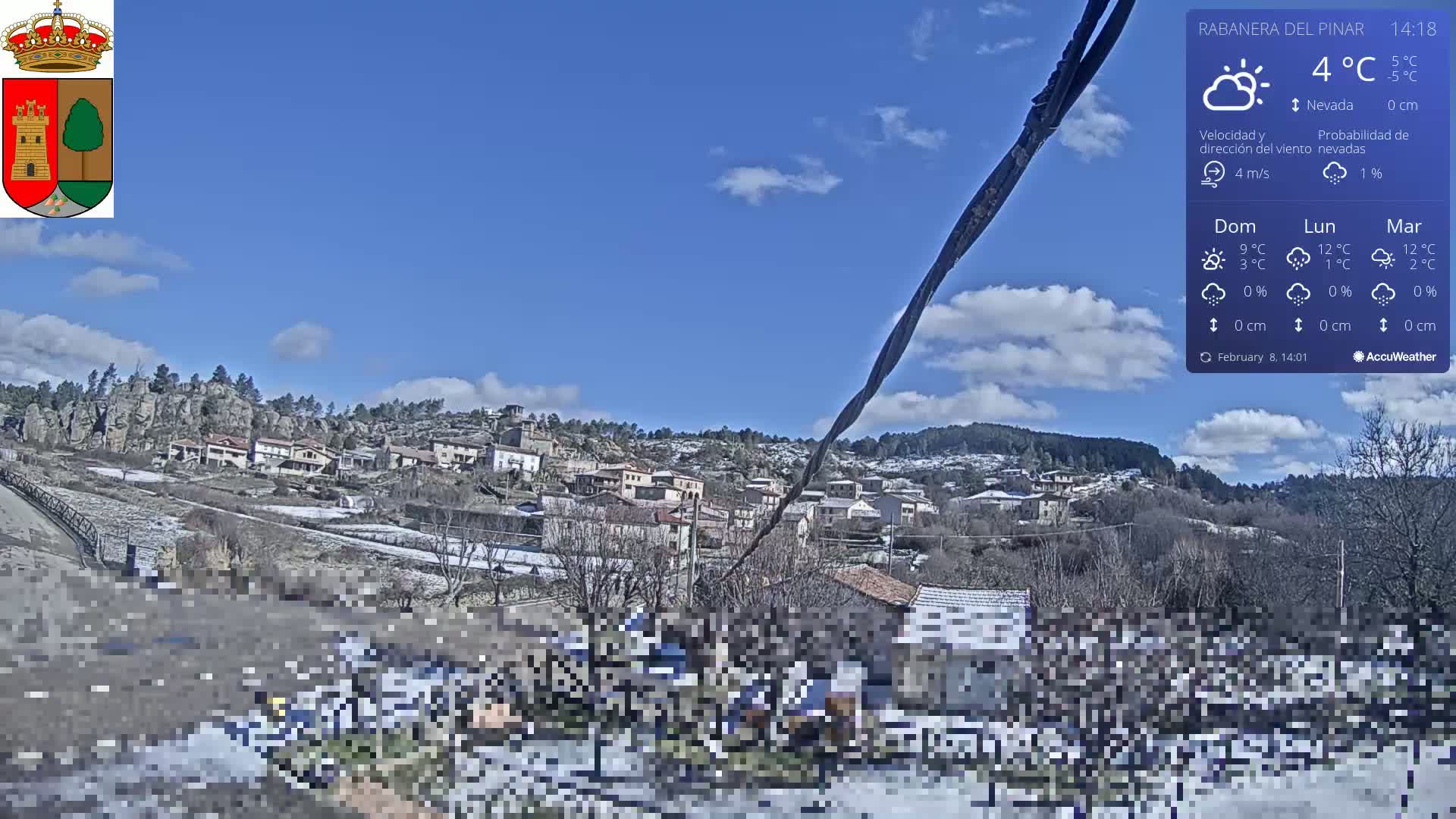 A small village nestled in a hilly landscape with patches of snow on the ground under a mostly sunny sky.