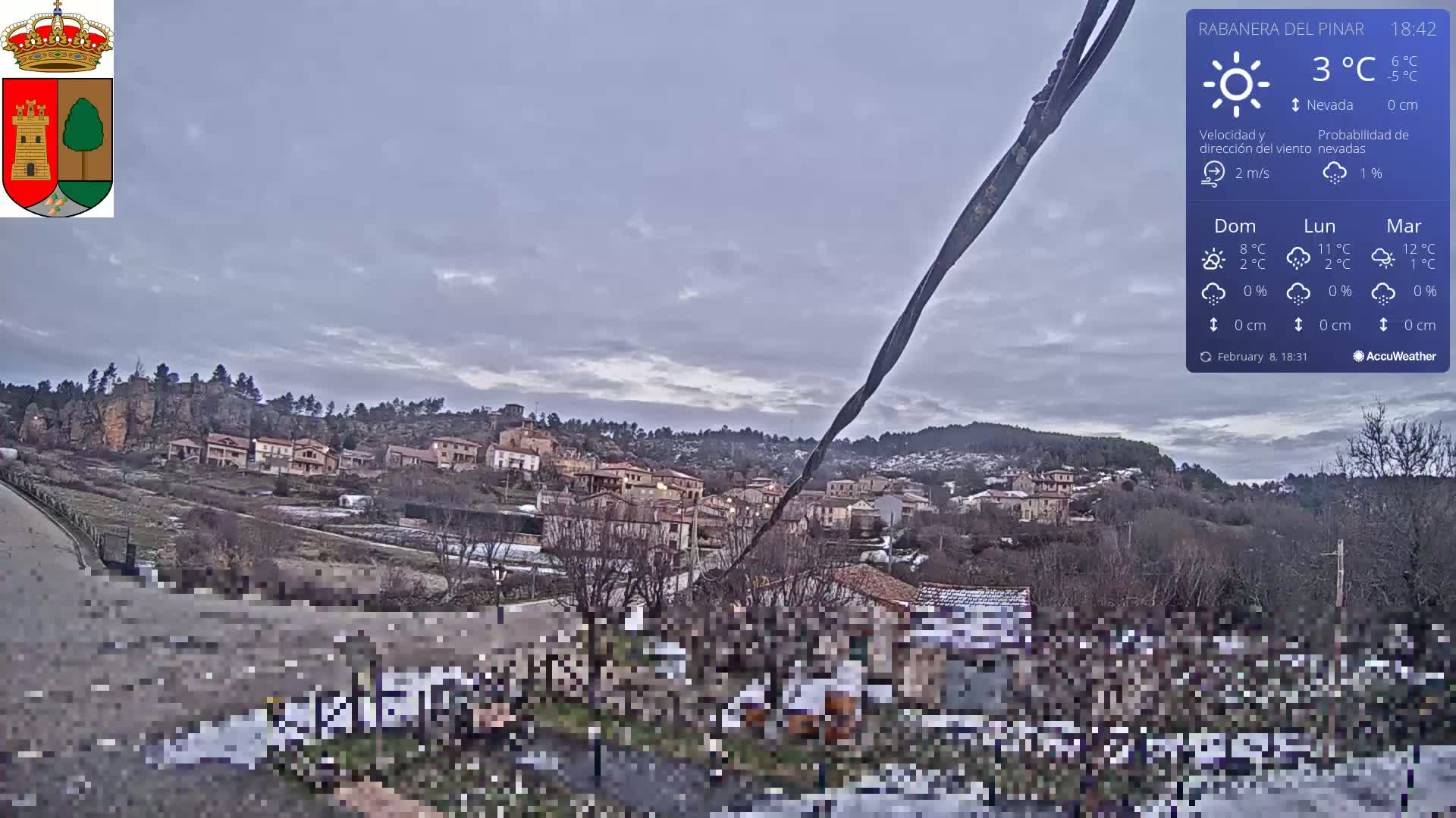 A small village nestled in a hilly landscape under an overcast sky, with some snow visible on the ground.