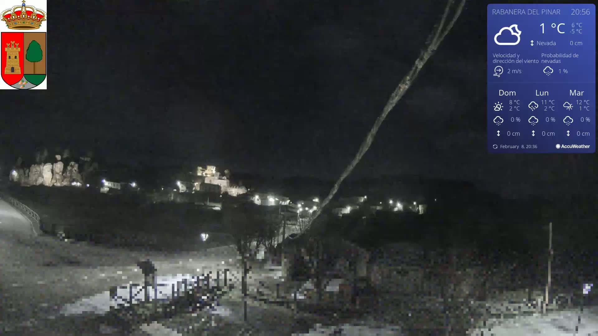 A nighttime view of a snow-covered village under a dark, clear sky with light snowfall.