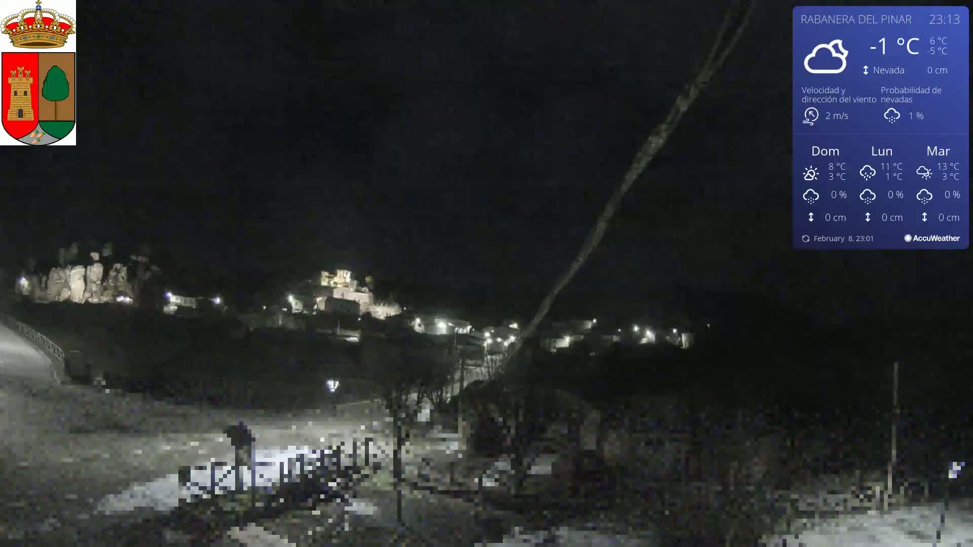 A nighttime view of a small town nestled in a dark landscape under a slightly snowy sky.