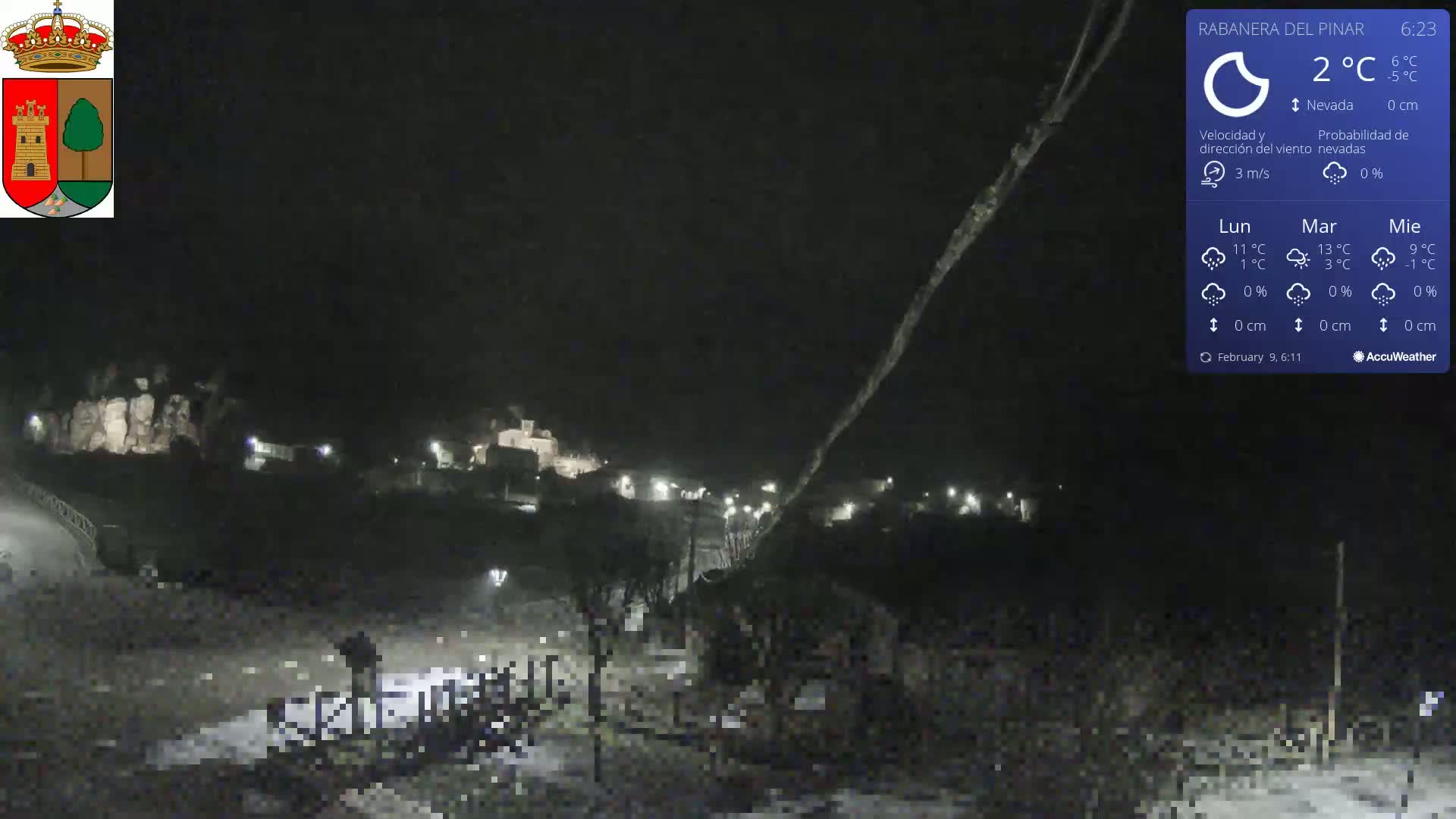 A nighttime, snowy scene shows a small village nestled in a valley under a dark sky.