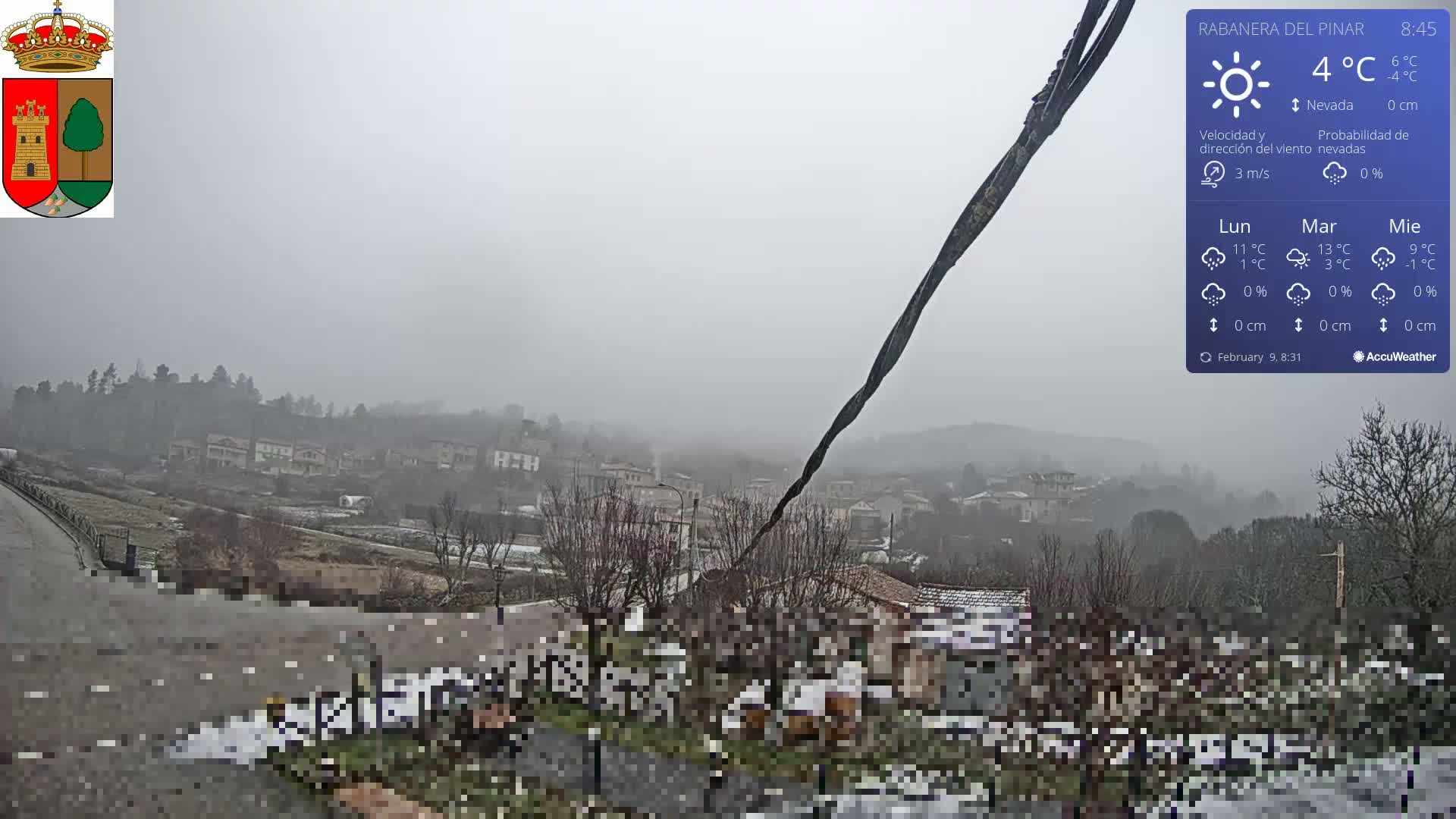 A foggy, snowy scene overlooks a small town nestled in a valley, with a few scattered houses and trees visible.