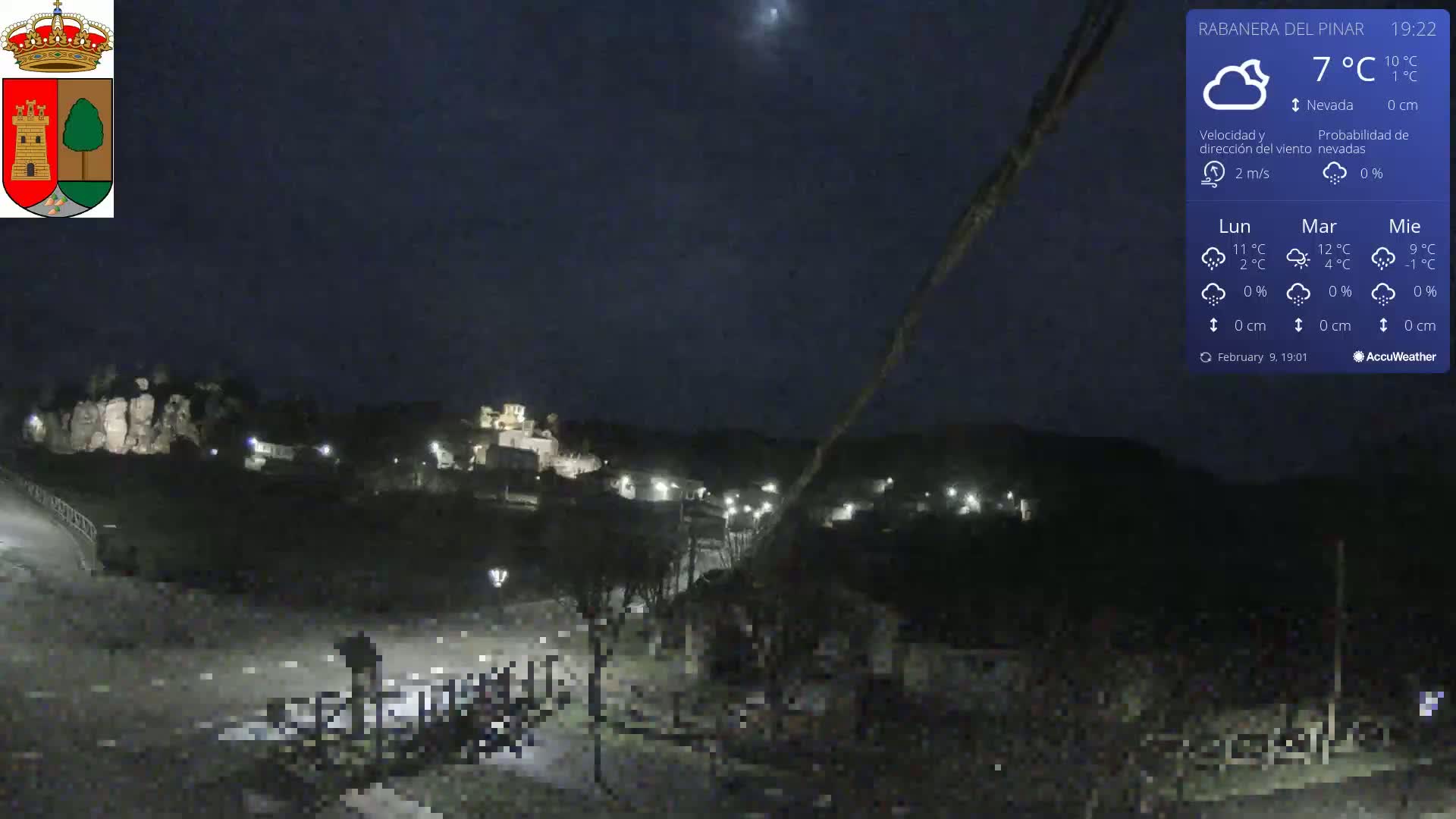 A nighttime view of a small town nestled in a valley under a clear, dark sky with light snowfall.
