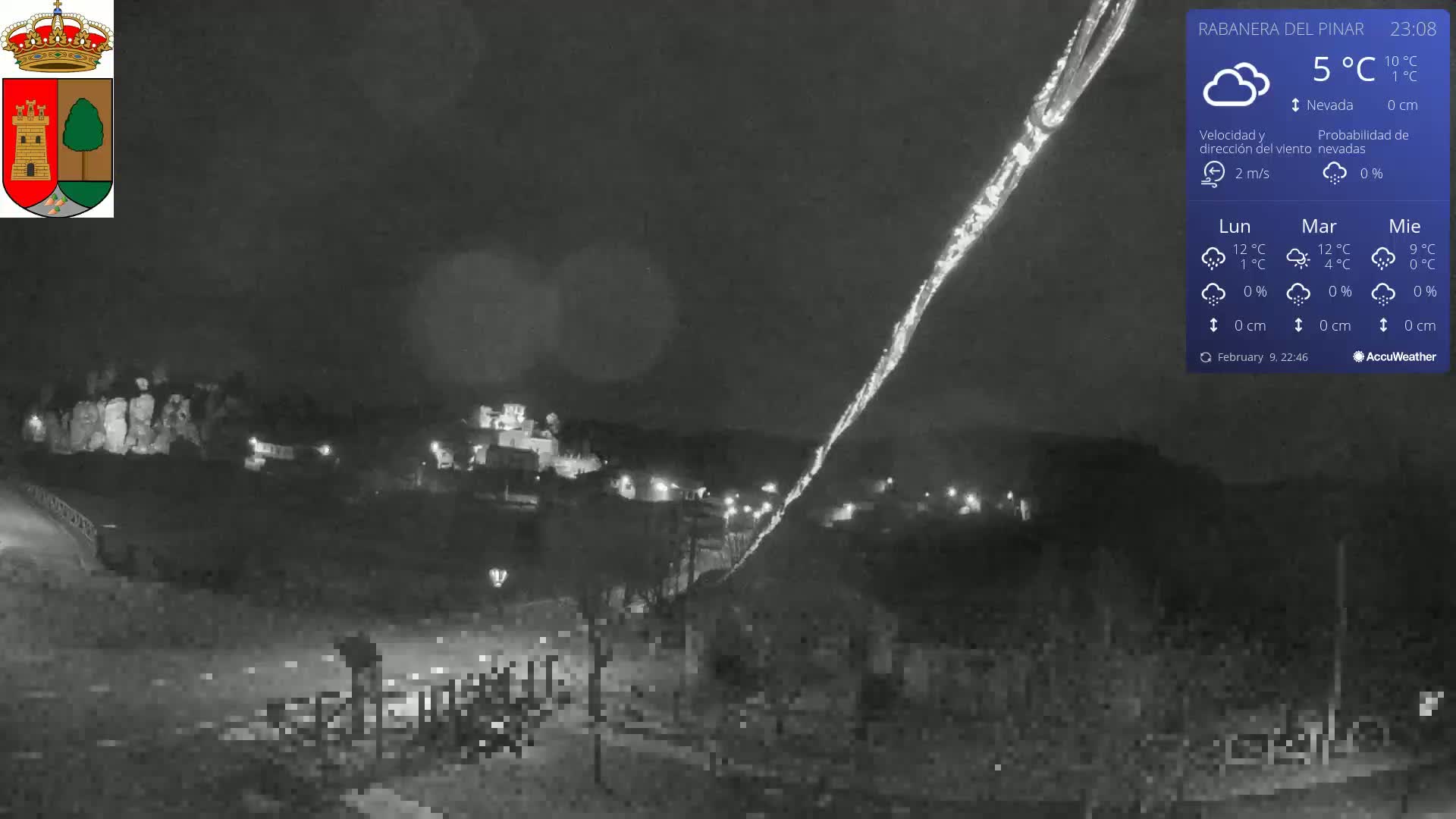A nighttime, low-light view of a town with a light snow fall, showing a long, bright streak across the dark sky.