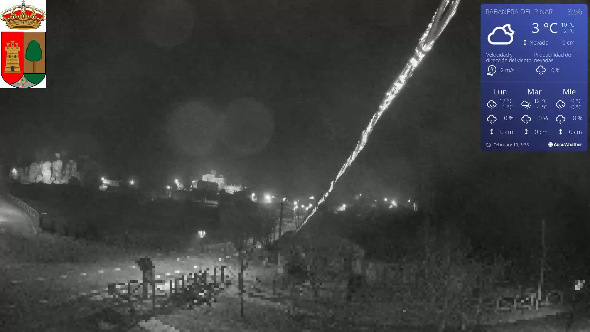 A nighttime, low-light view of a town illuminated by streetlights, with a bright streak of light in the sky, under cloudy skies.