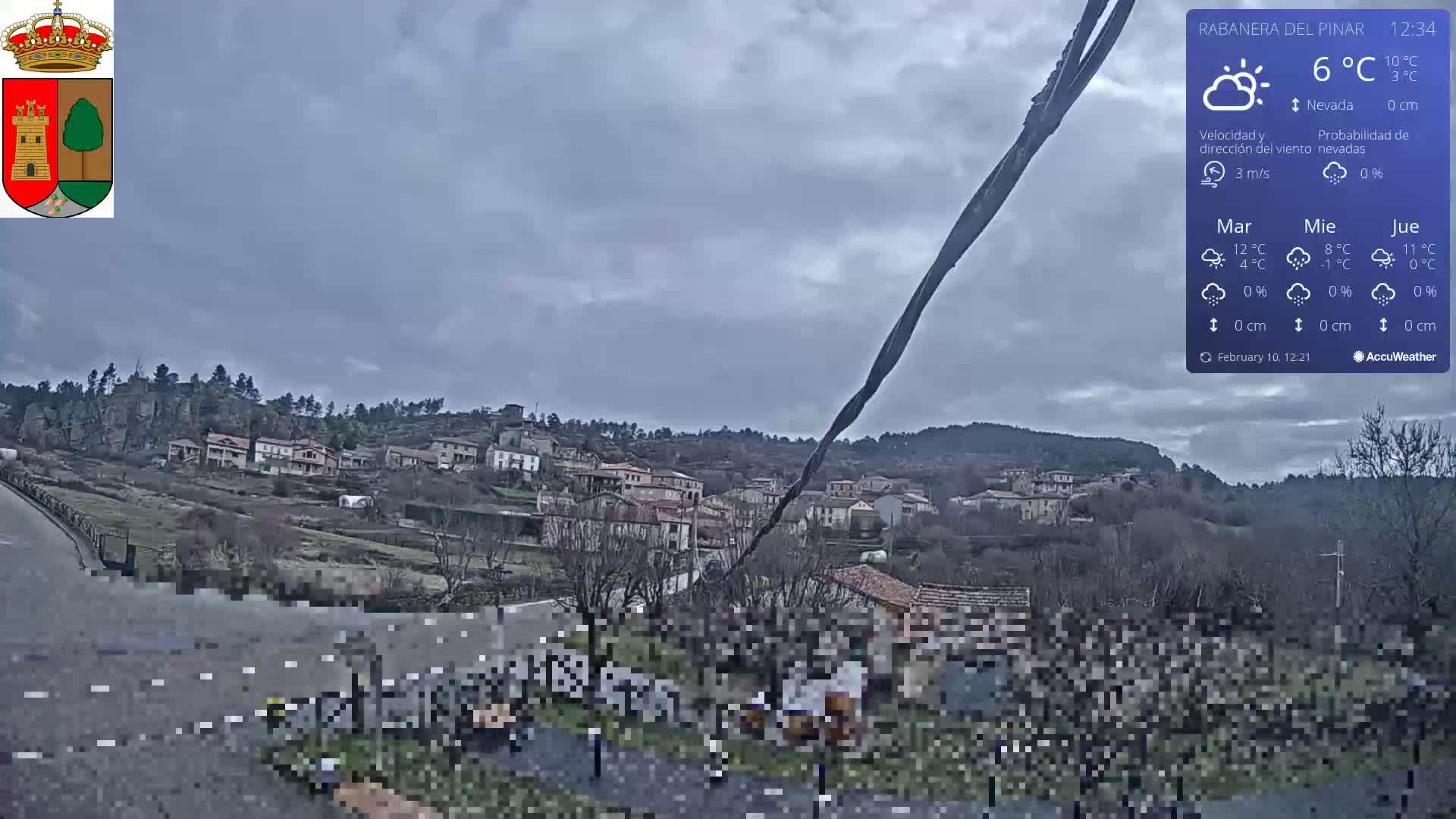 A small village nestled in a hillside is viewed from a distance on an overcast day with a temperature of 6°C.