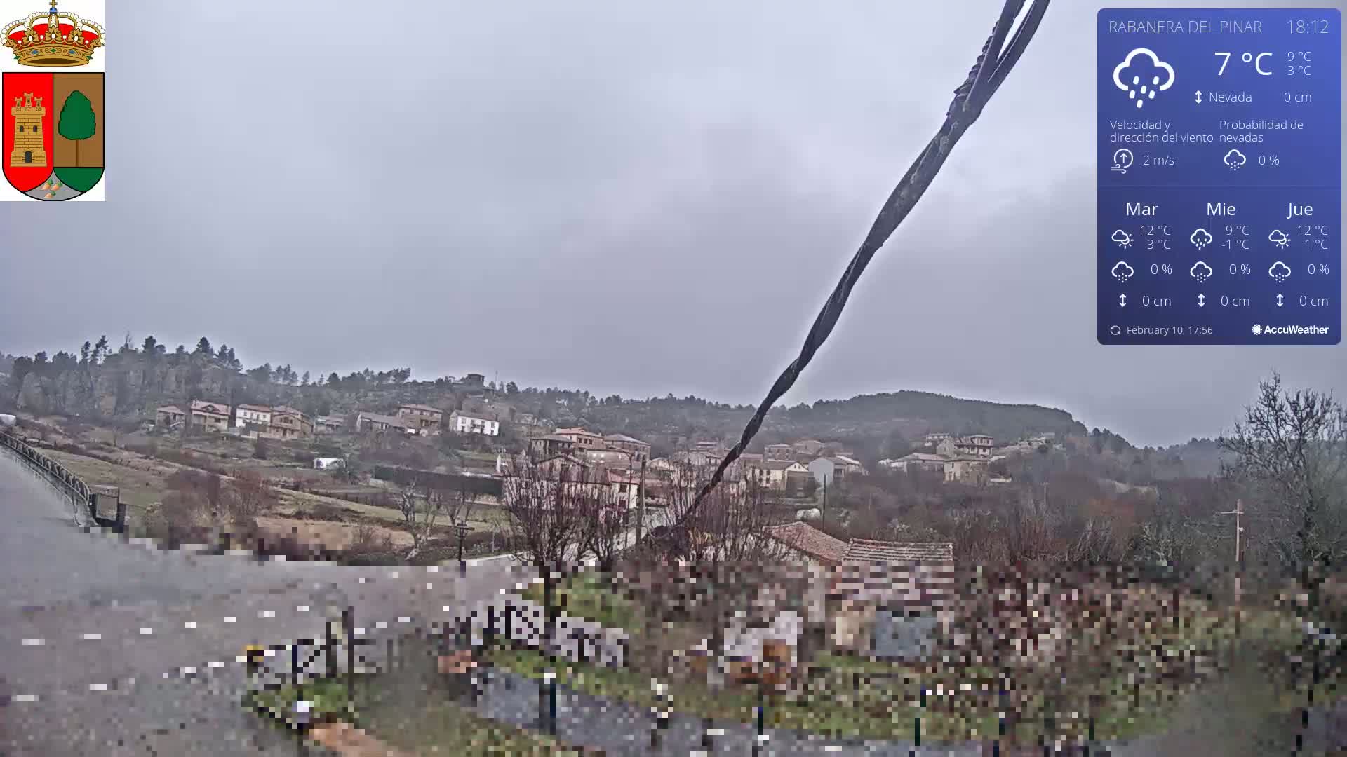 A view of a small town nestled in a hillside under an overcast sky, with light rain or snow falling.