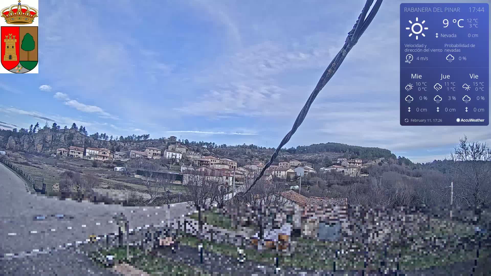 A partly cloudy sky over a small village nestled in a hilly landscape.